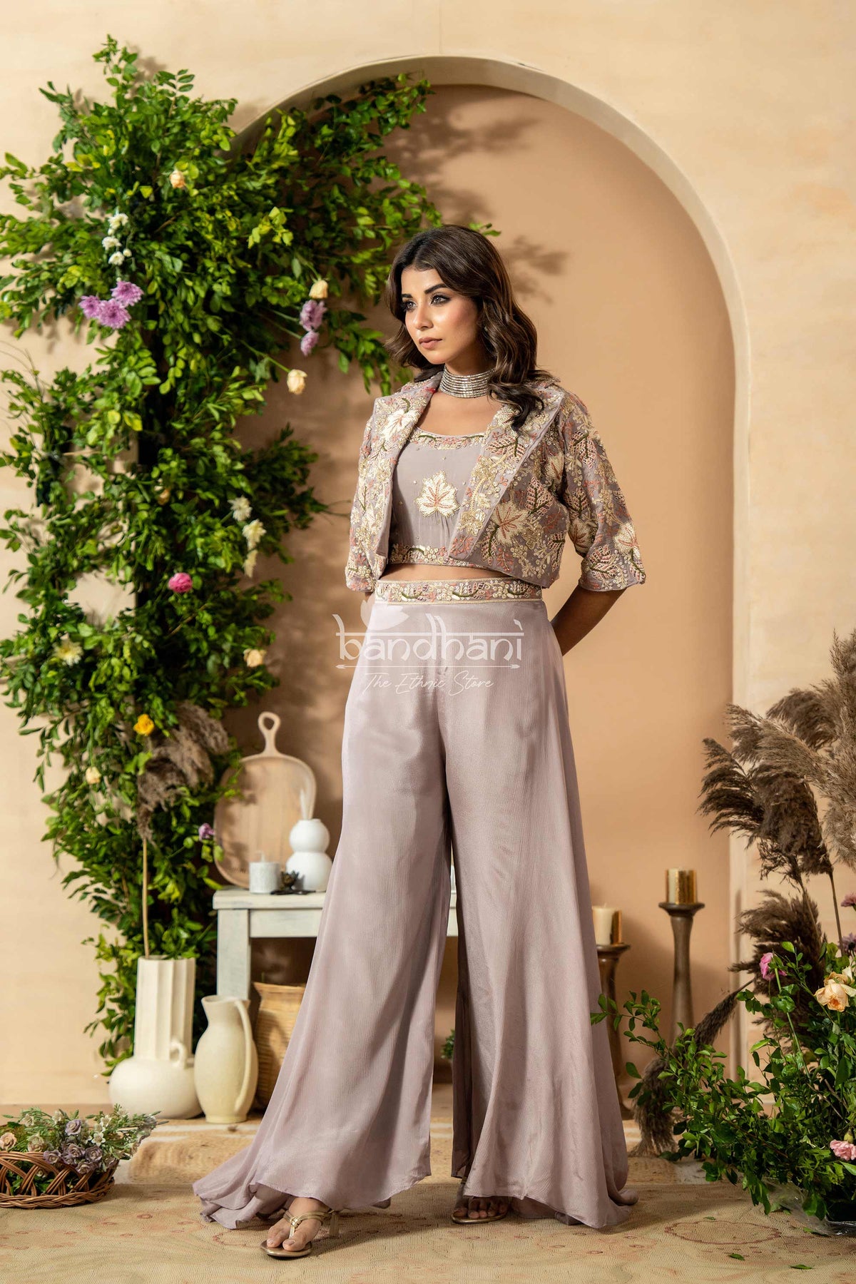 Woman in a stylish outfit standing in a decorated indoor setting with plants and archway.
