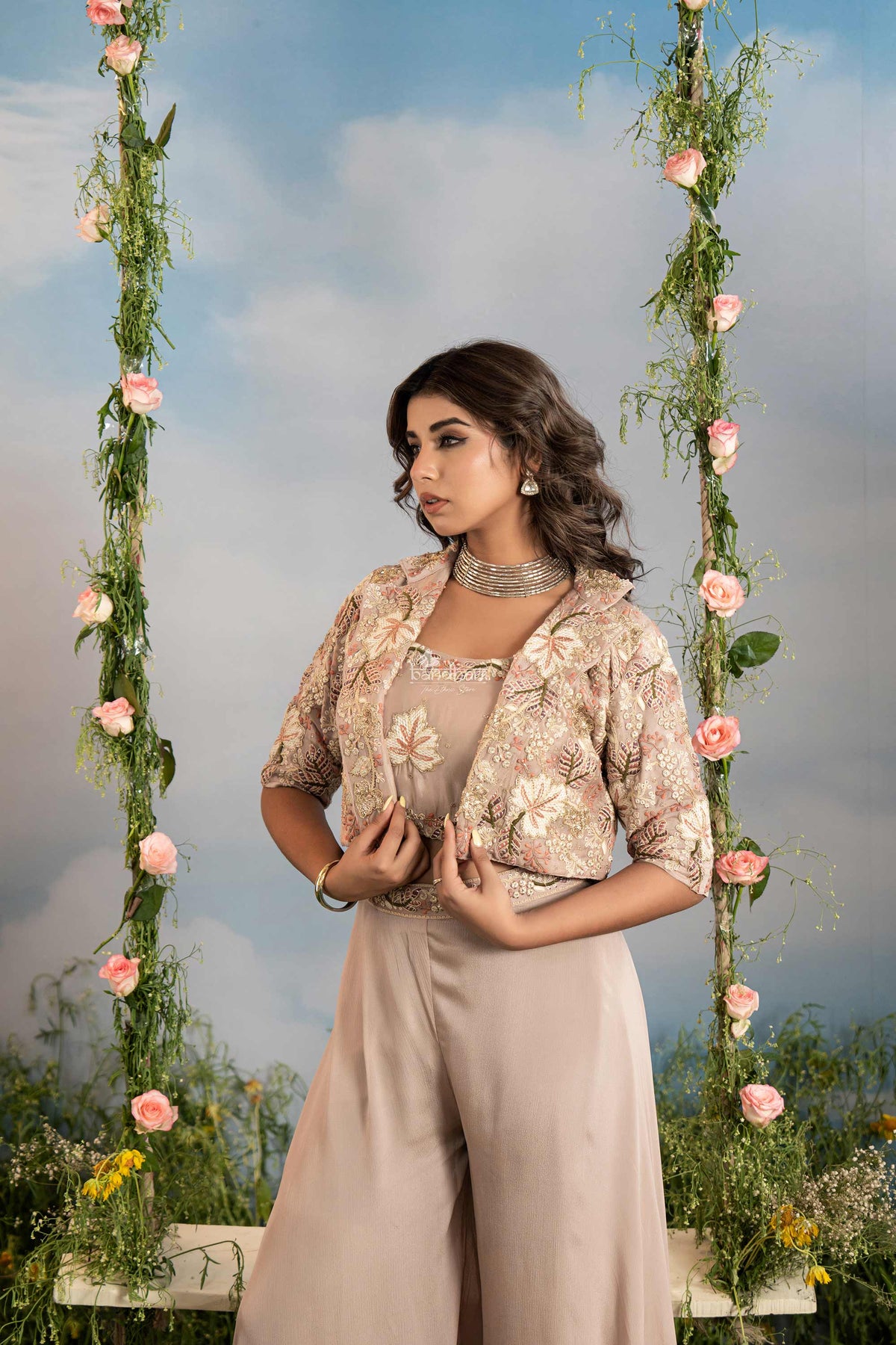 Woman in a floral top and beige pants sitting on a swing decorated with flowers and greenery.