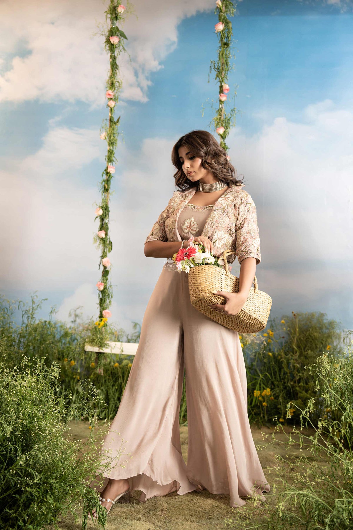 Woman in a beige outfit standing on a grassy field with a swing and flowers in the background