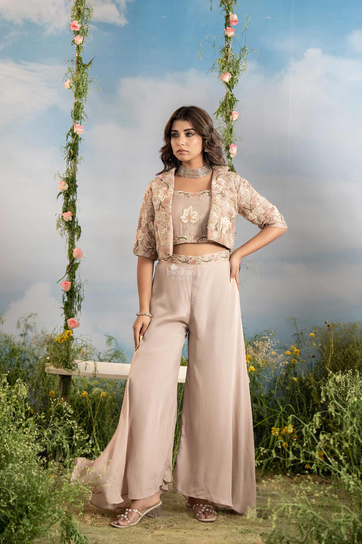 Woman in a beige outfit standing on a grassy area with floral decorations.