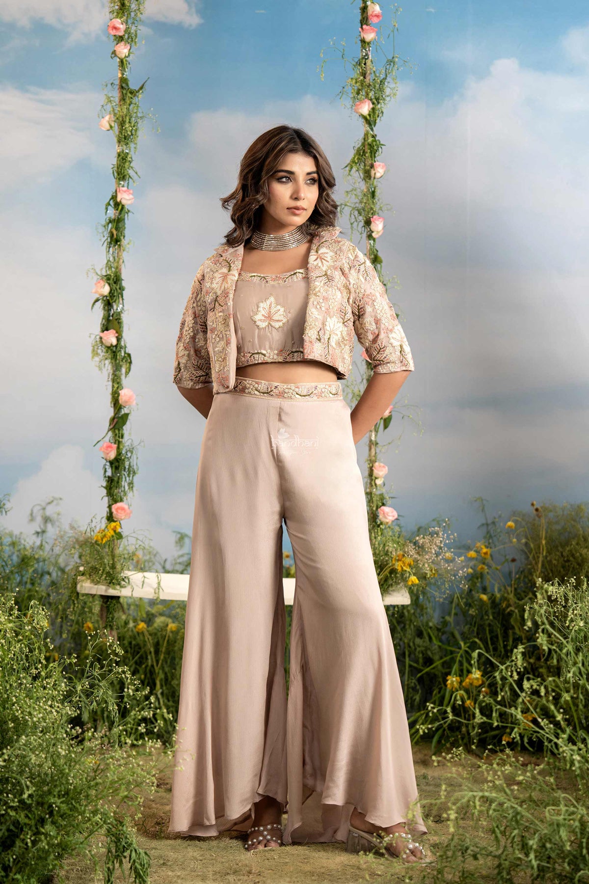 Woman in a beige outfit standing on a swing with floral decorations against a blue sky.