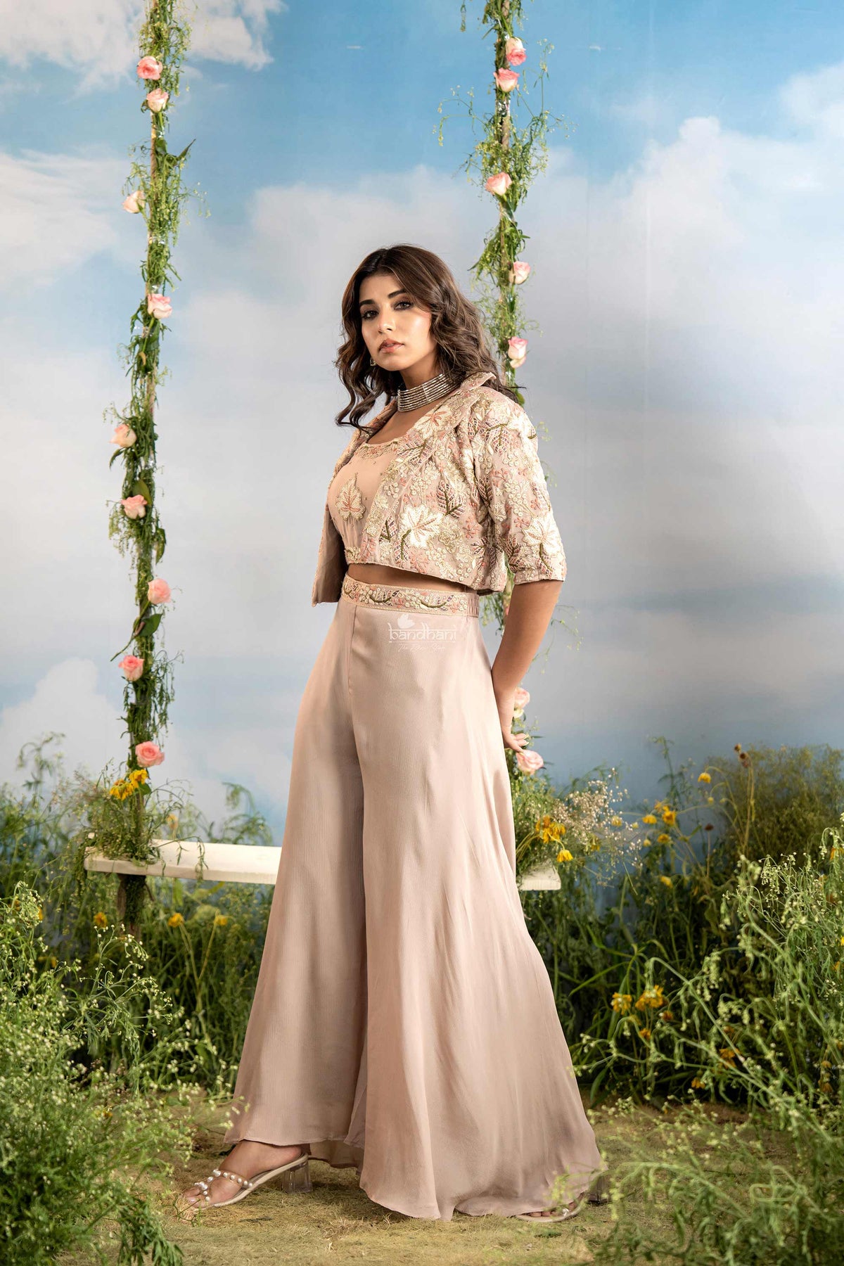 Woman in a flowing outfit standing in a garden with floral decorations.
