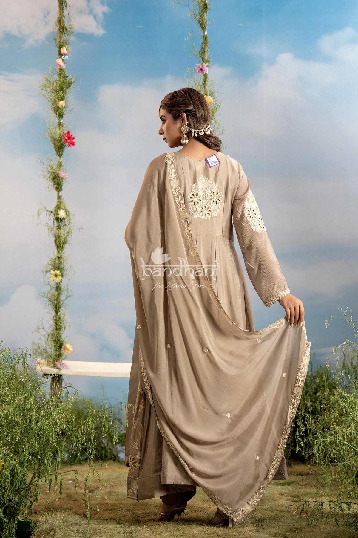 Woman in a beige embroidered traditional outfit standing on a swing with a scenic background