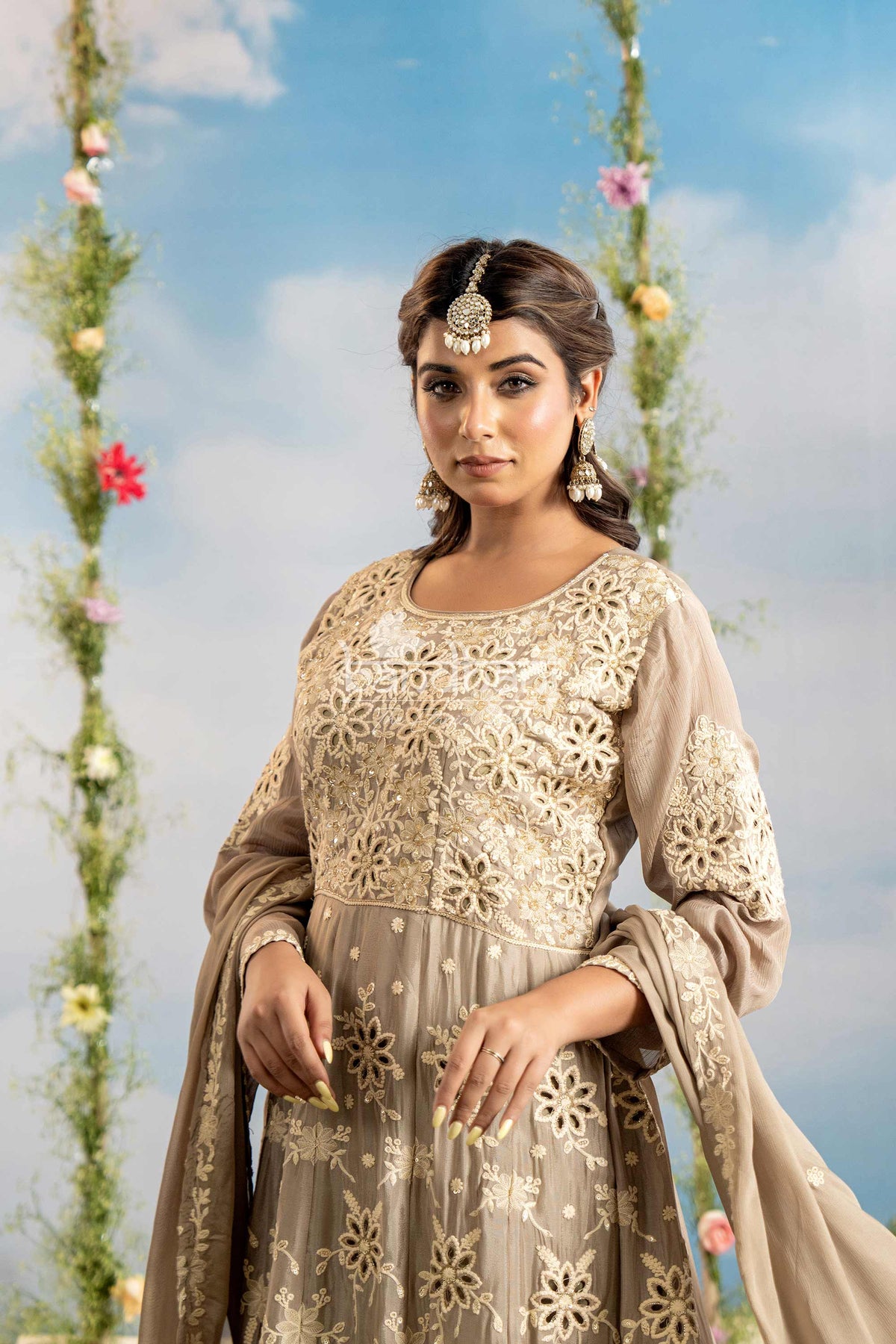 Woman in a beige embroidered traditional outfit with floral decorations in the background