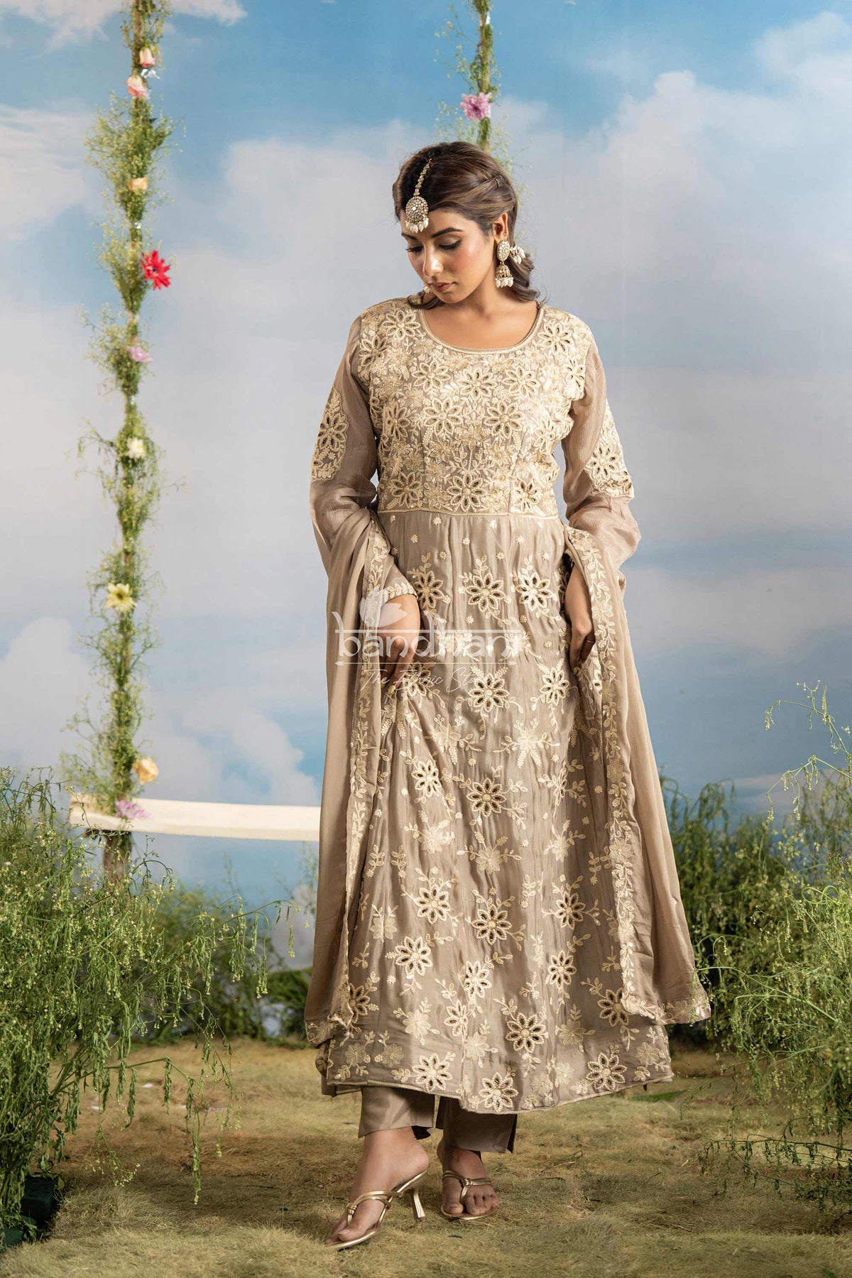 Woman in a traditional outfit standing outdoors with greenery and a swing in the background