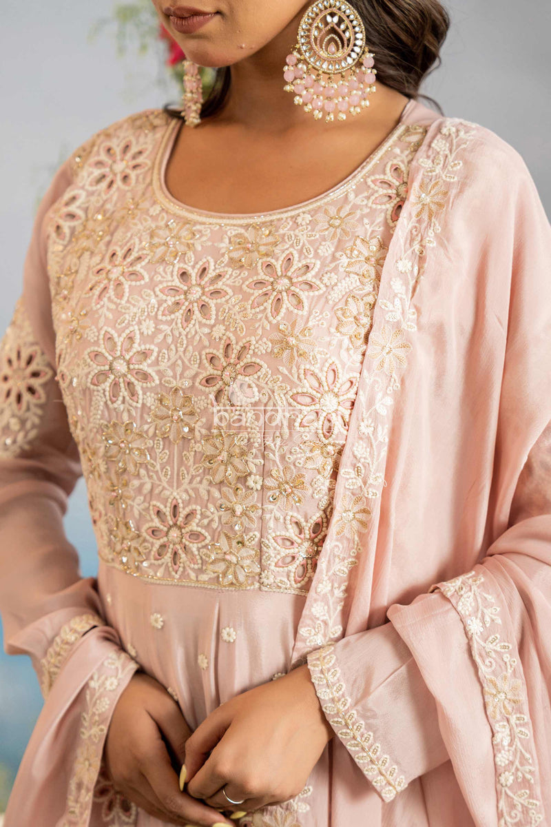 Woman wearing a pink embroidered outfit with gold detailing against a light gray background