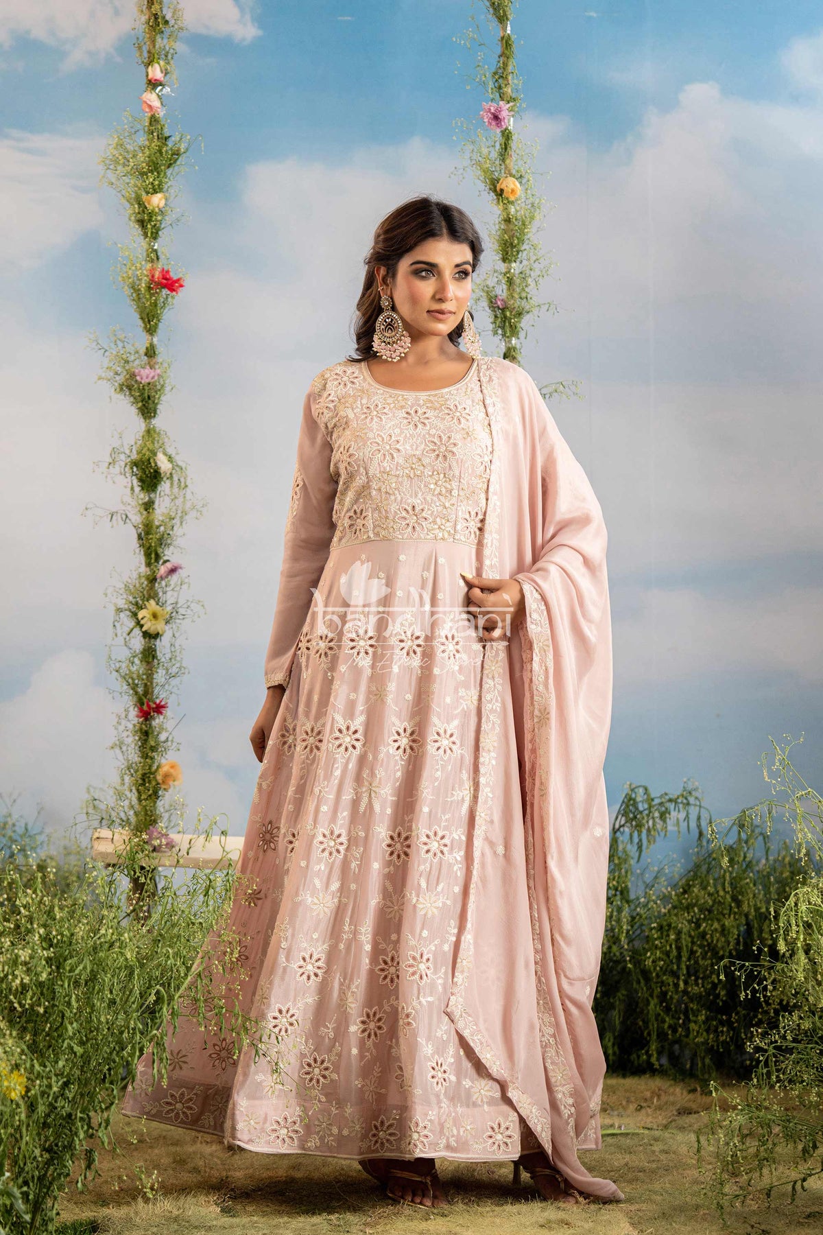 Woman in a pink traditional outfit standing outdoors with floral decorations and greenery.