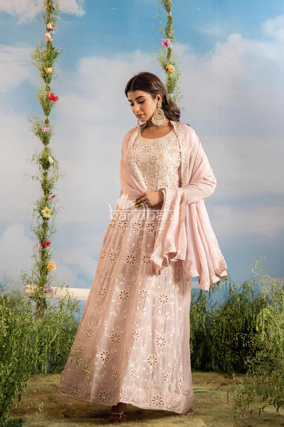 Woman in a pink traditional outfit standing outdoors with a floral swing and greenery in the background