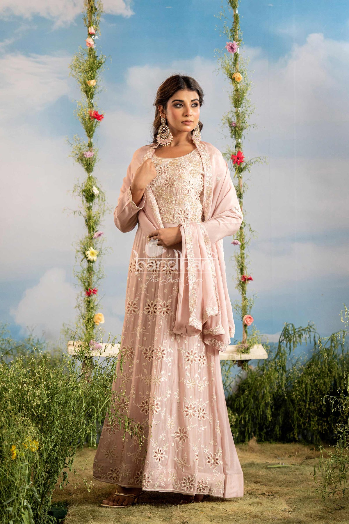 Woman in a pink traditional outfit standing on a swing with floral decorations against a blue sky.