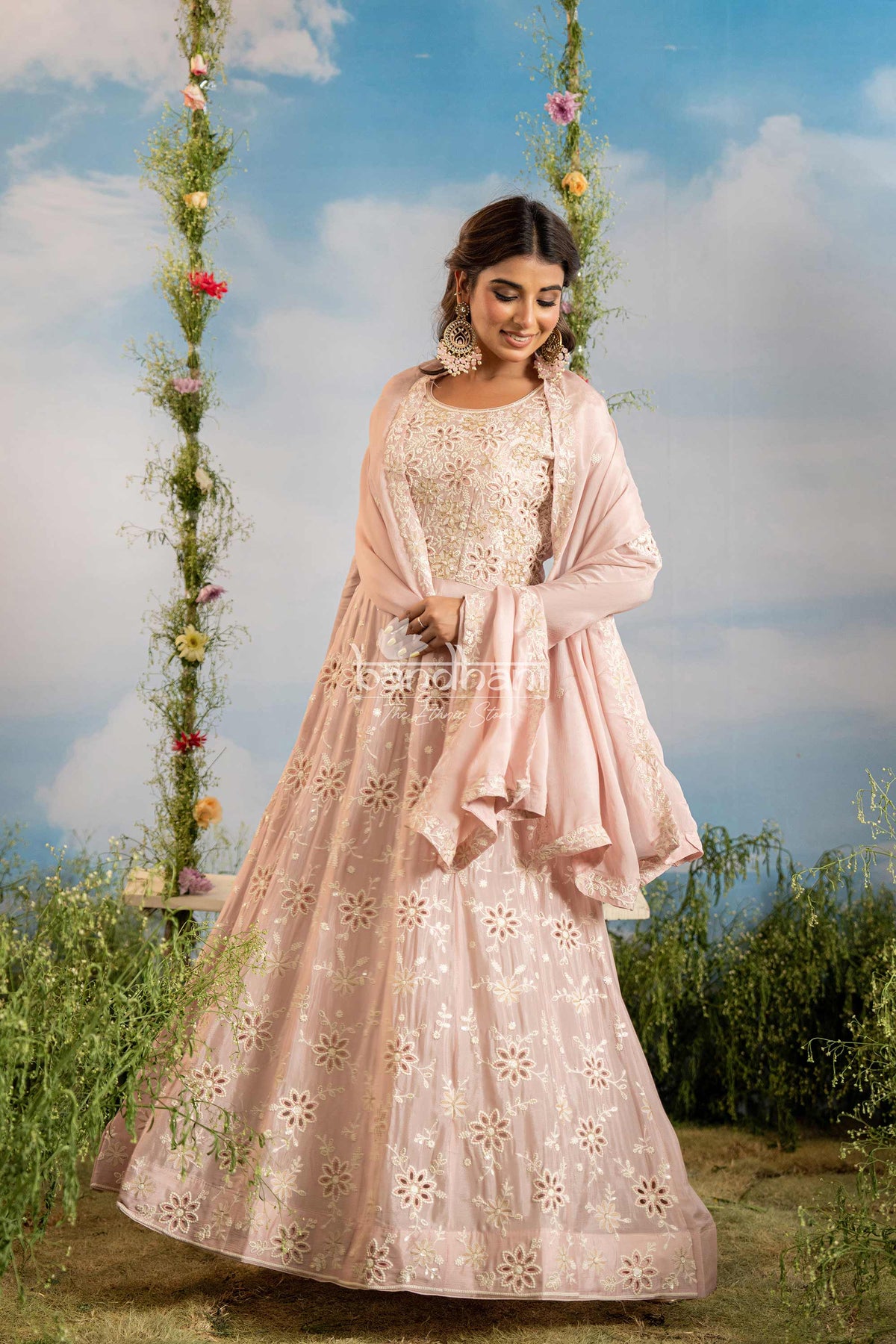 Woman in a pink traditional outfit with floral patterns standing outdoors against a blue sky.
