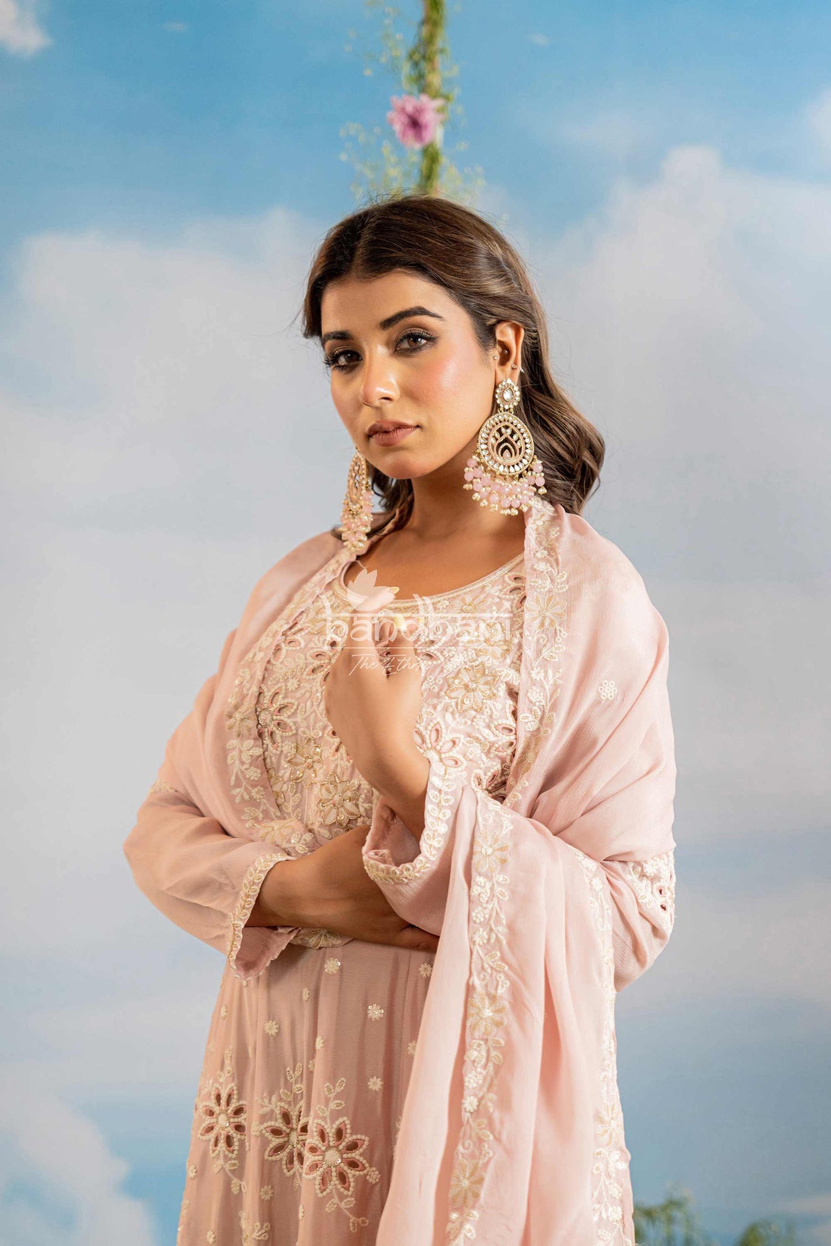 Woman wearing a light pink traditional outfit with intricate designs against a blue sky.