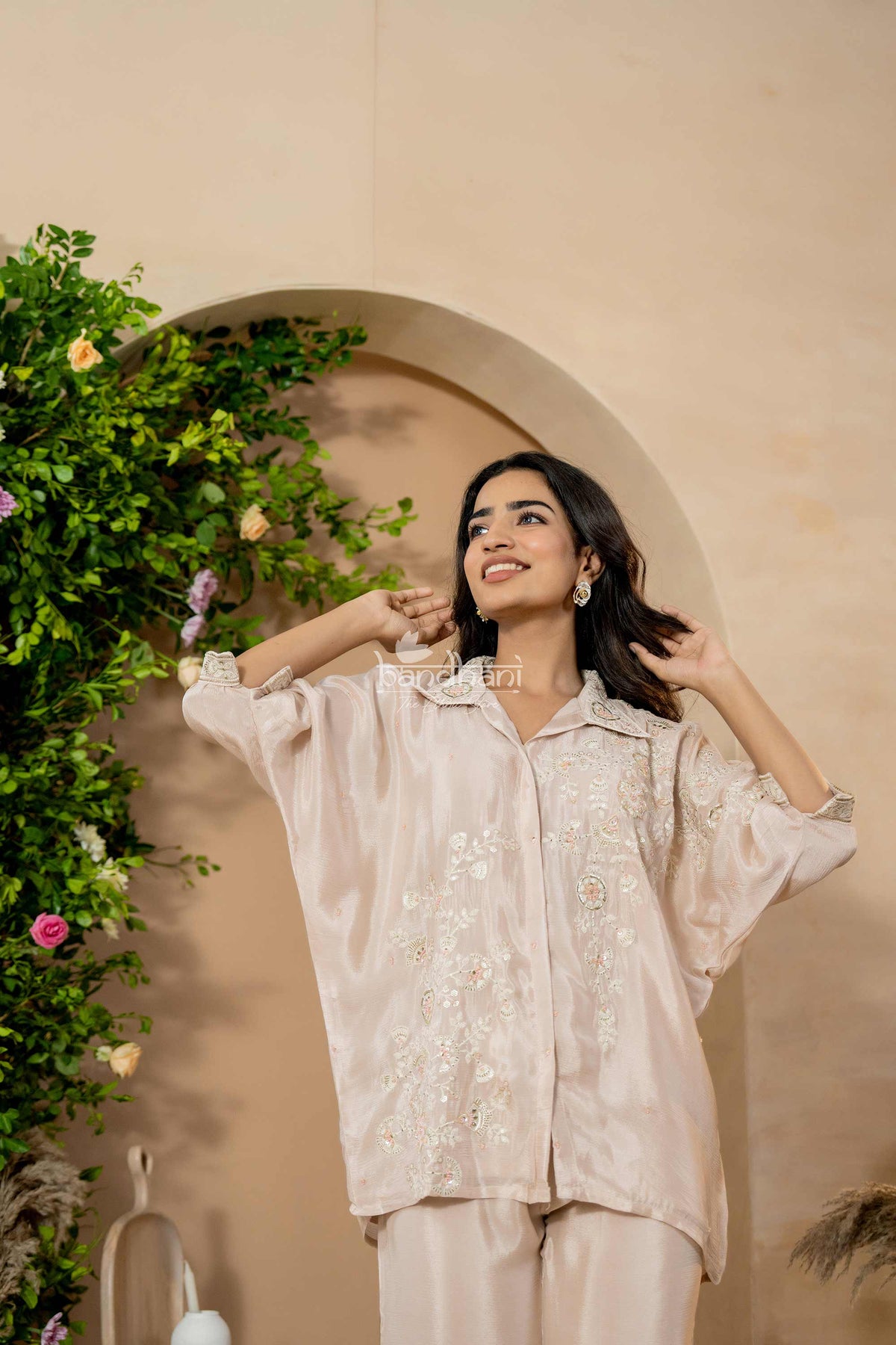 Woman in a light pink outfit standing in front of a decorative arch with greenery.