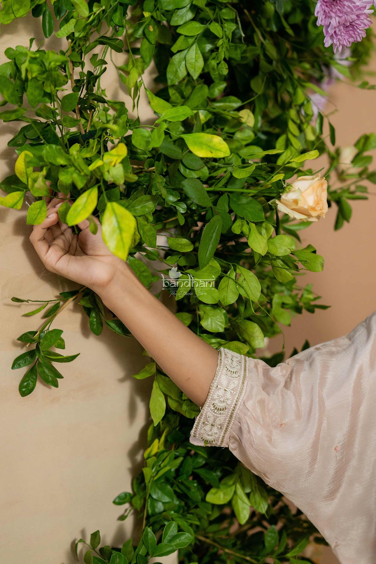 Person arranging green leaves and flowers against a beige wall