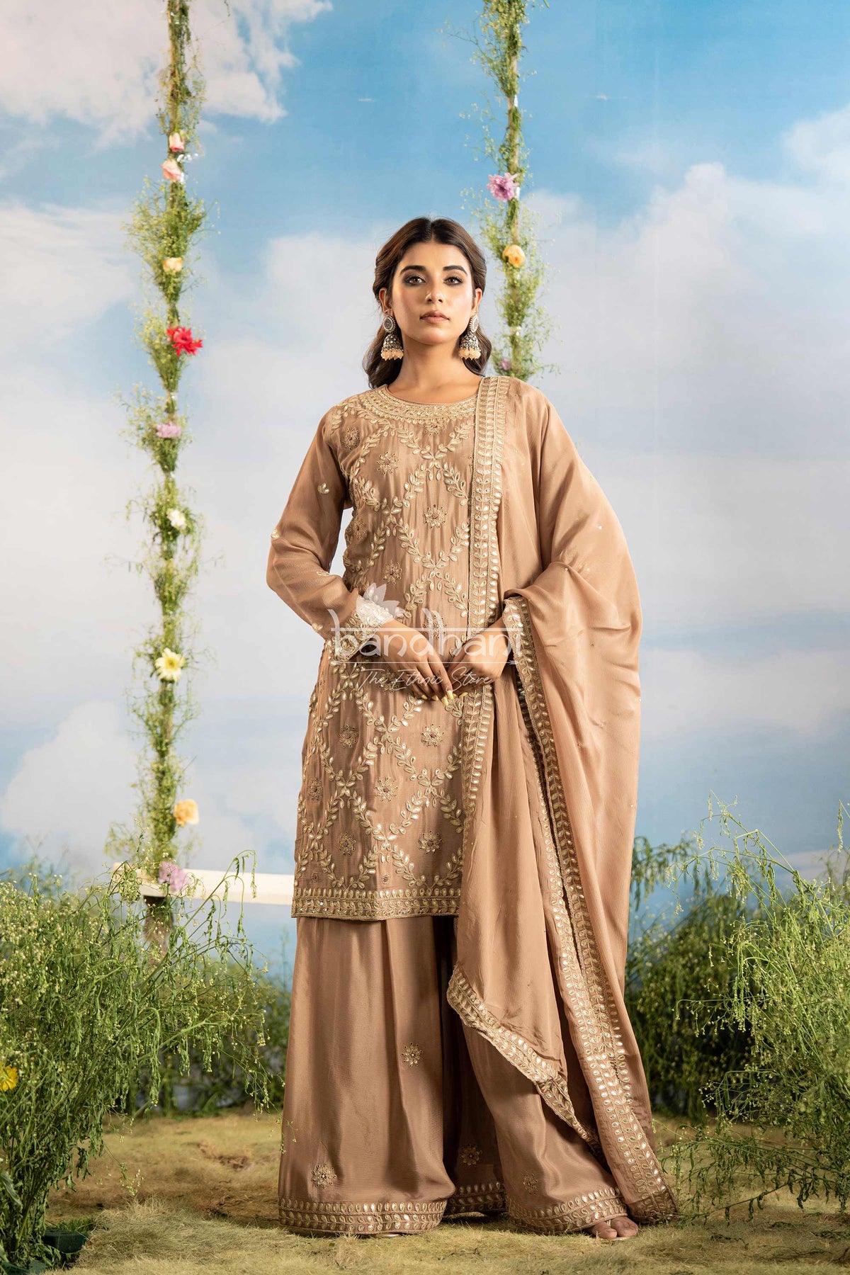 Woman in a traditional brown outfit with floral decorations against a scenic background