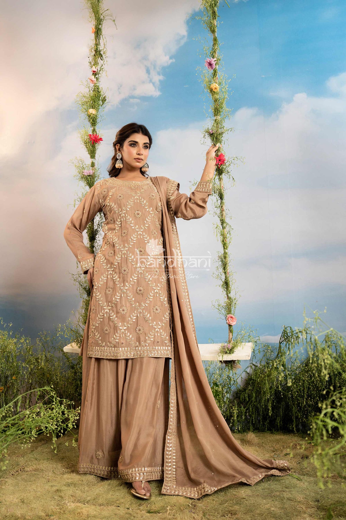 Woman in a traditional outfit with embroidered details, standing on a grassy area with a scenic background.