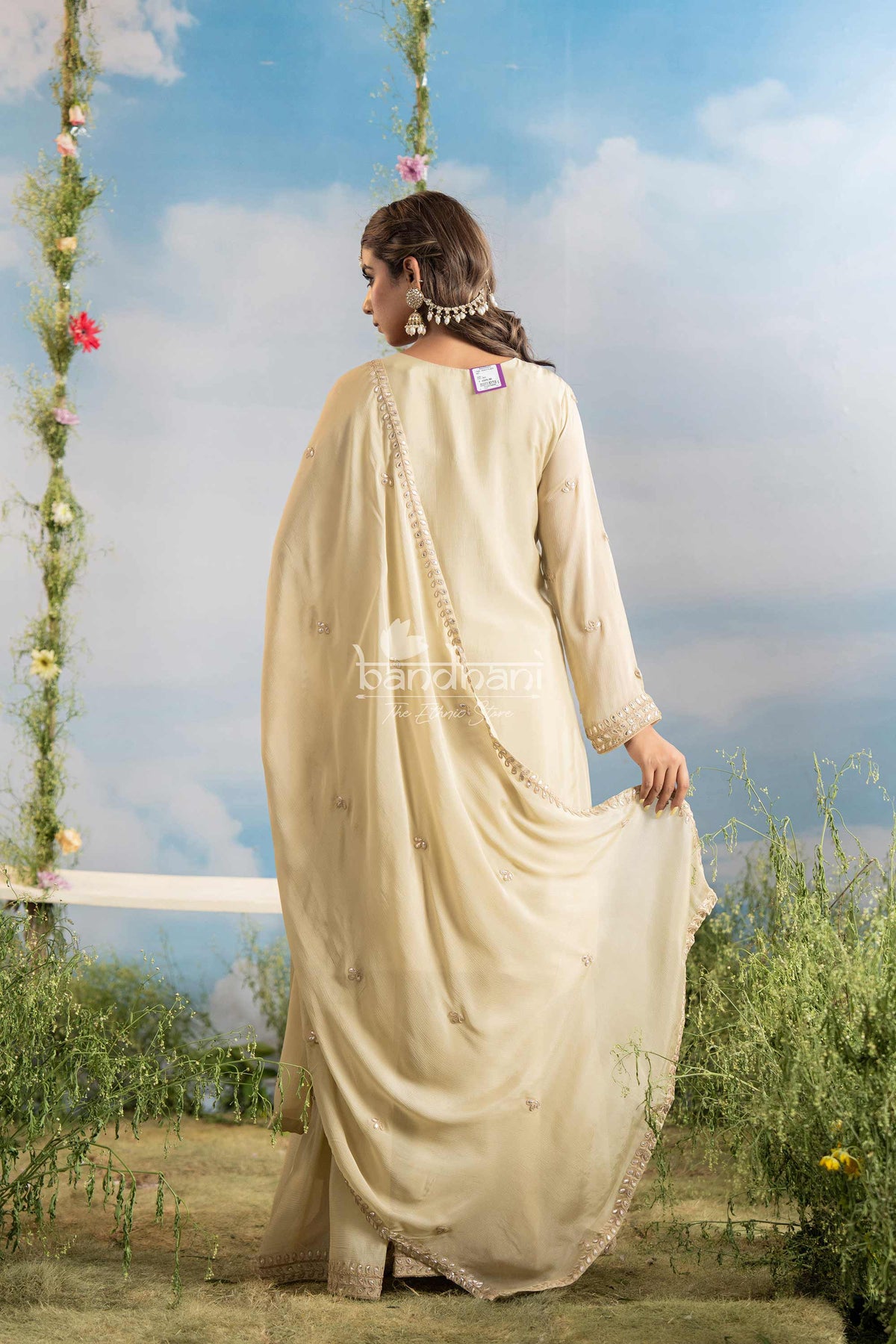 Woman in a beige saree standing outdoors with a scenic background