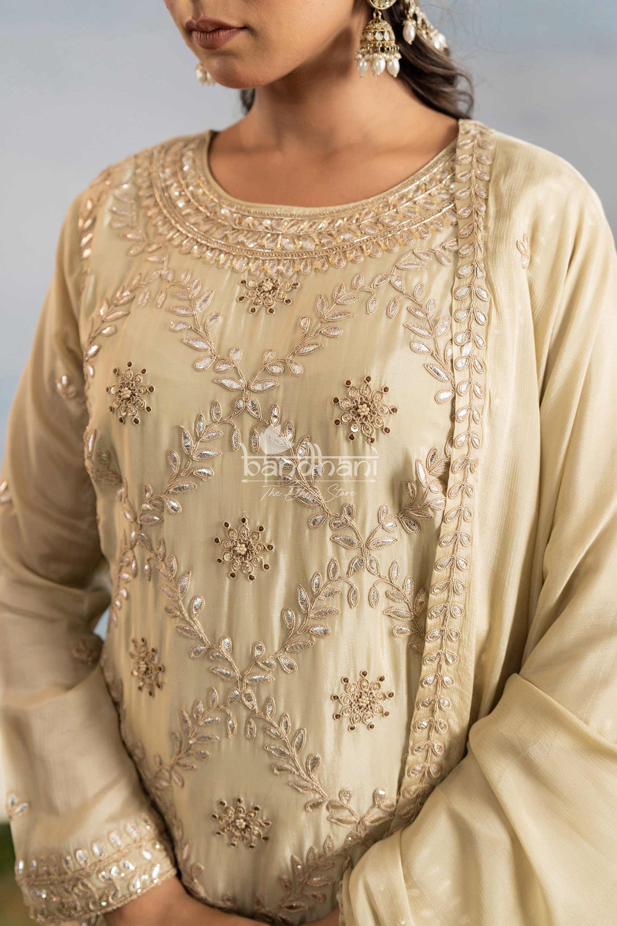 Beige embroidered traditional outfit with intricate designs on a plain background