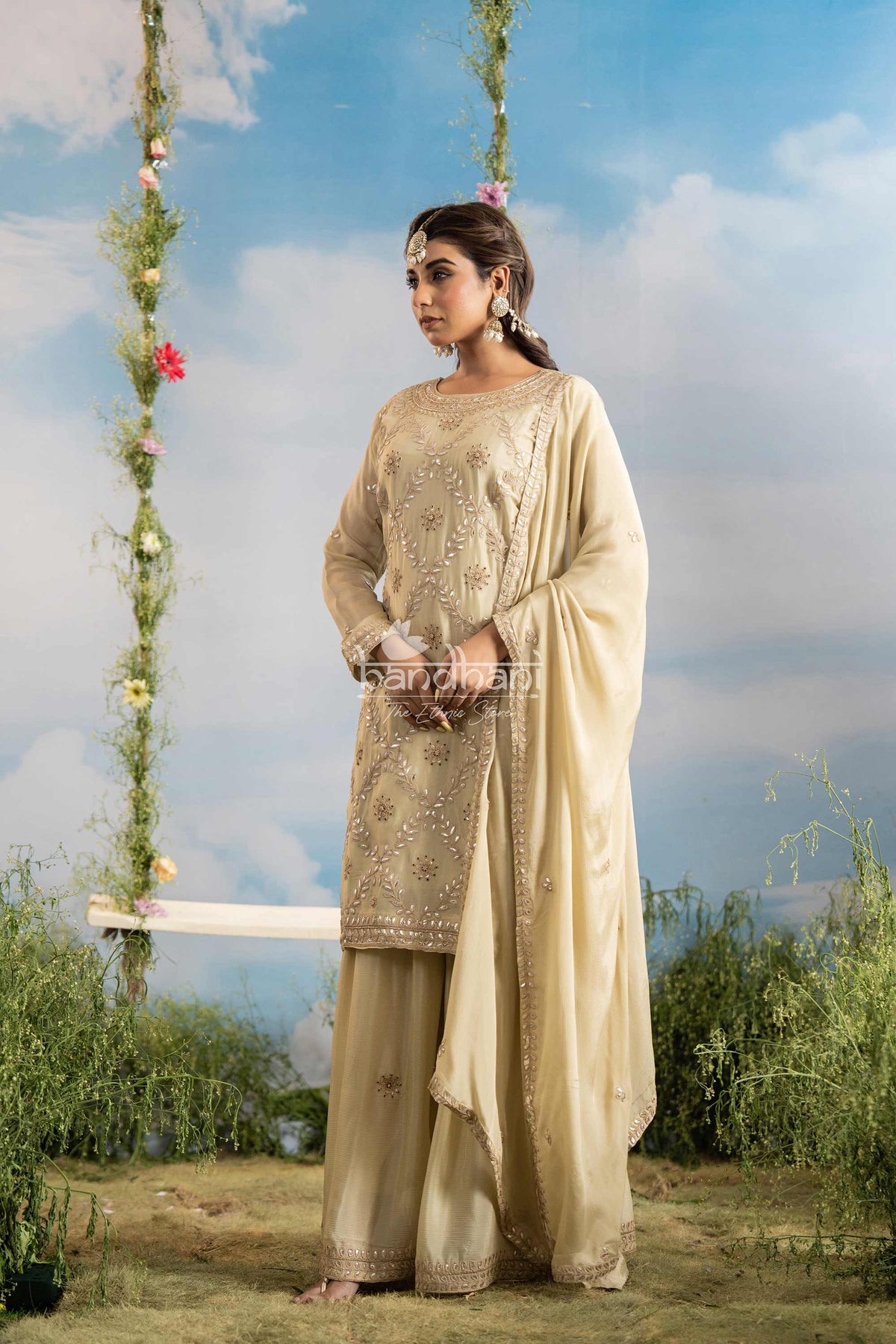 Woman in traditional beige outfit standing next to a floral swing with a scenic background