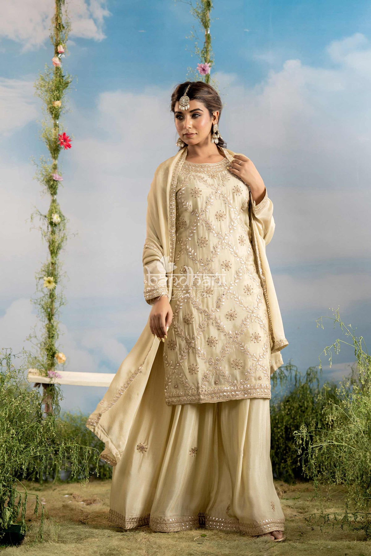 Woman in traditional beige outfit standing outdoors with a floral swing in the background