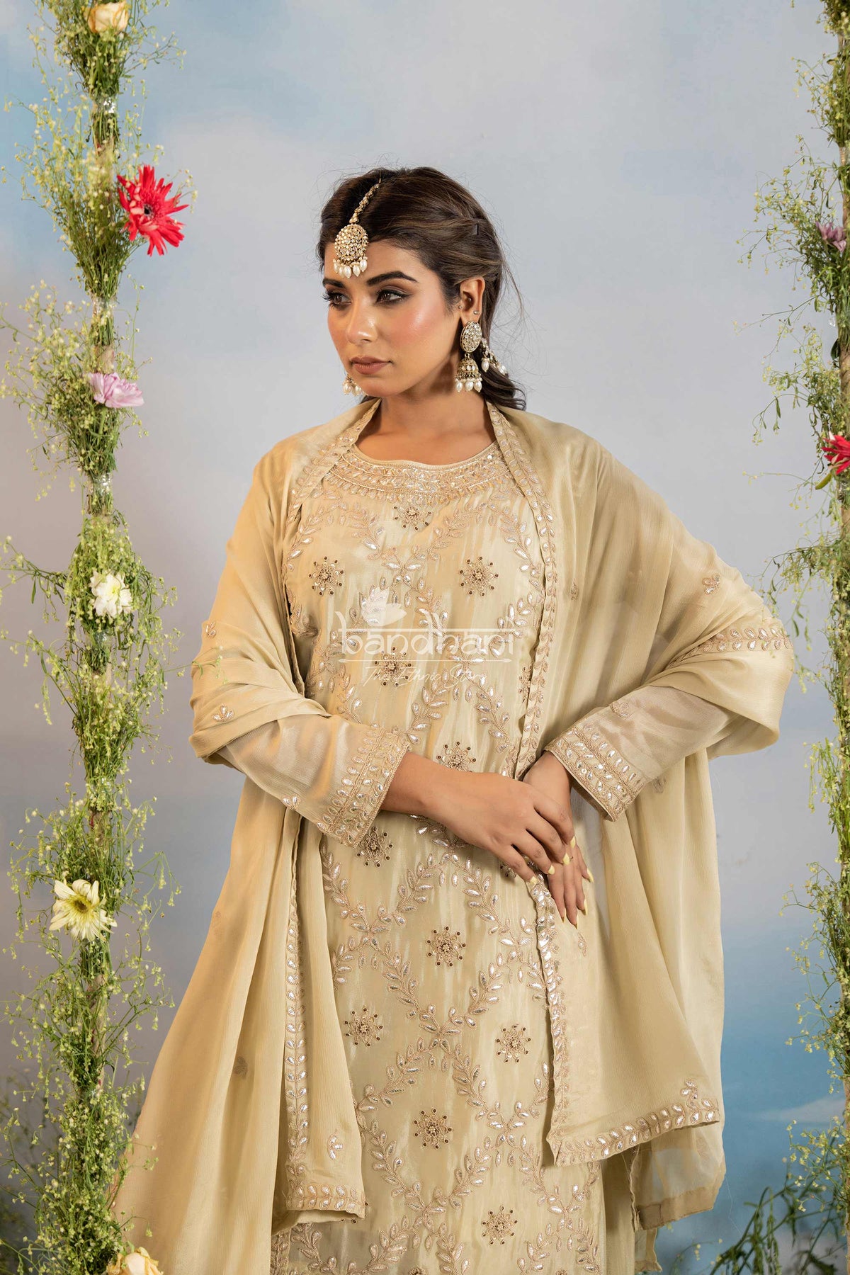 Woman in a beige embroidered outfit with floral decorations on a light blue background