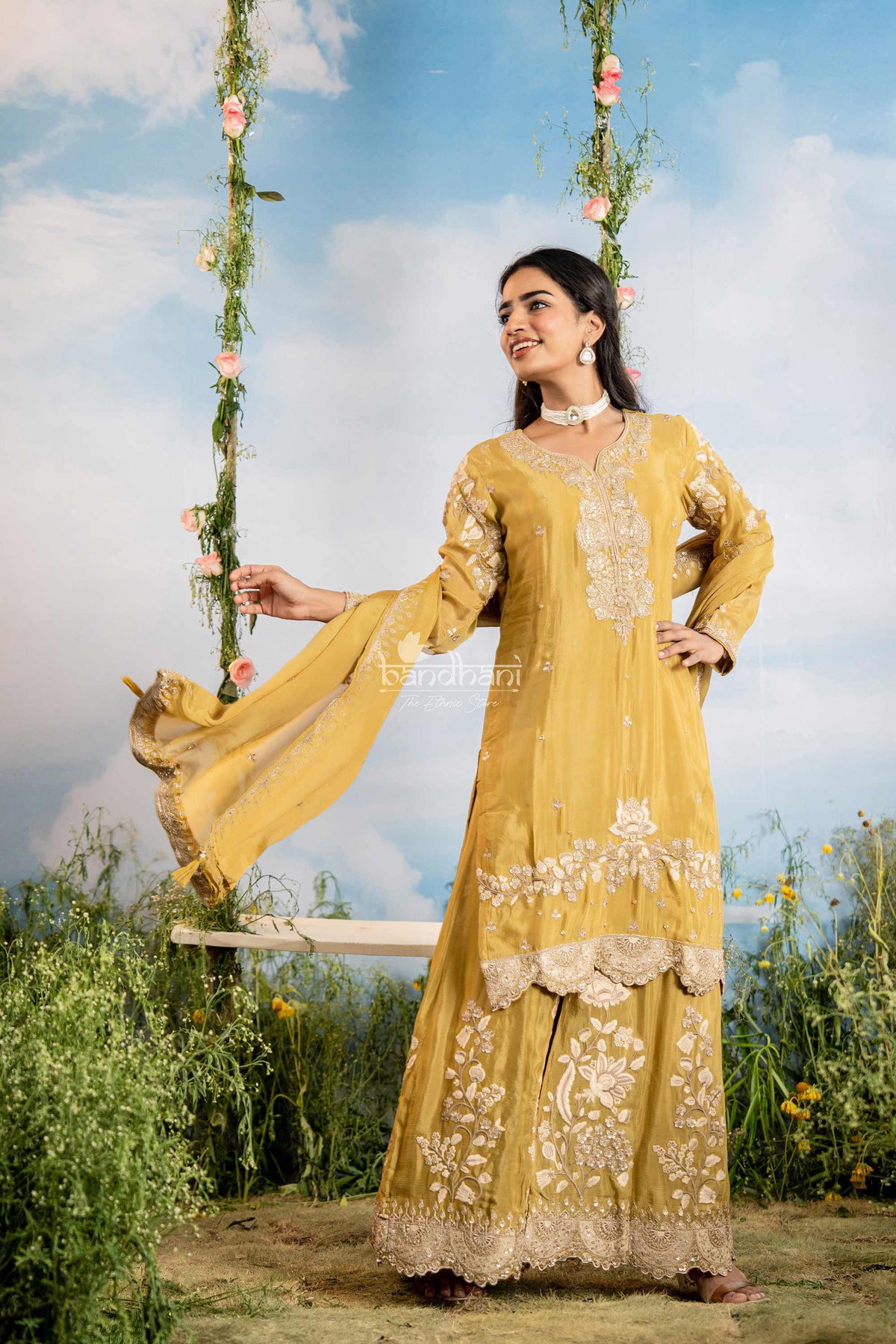 Woman in a yellow traditional outfit with floral decorations on a swing against a blue sky.