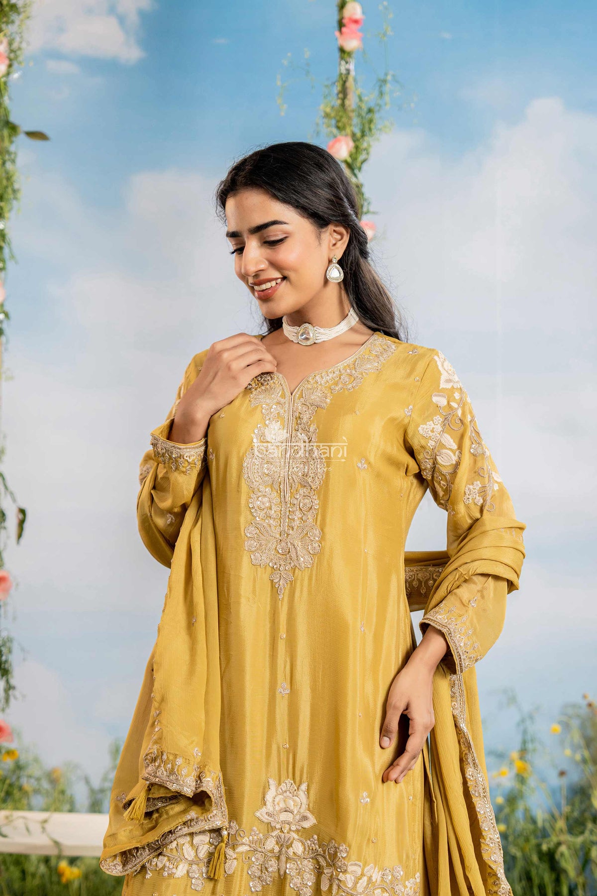 Woman in a yellow embroidered traditional outfit standing outdoors with a blue sky background