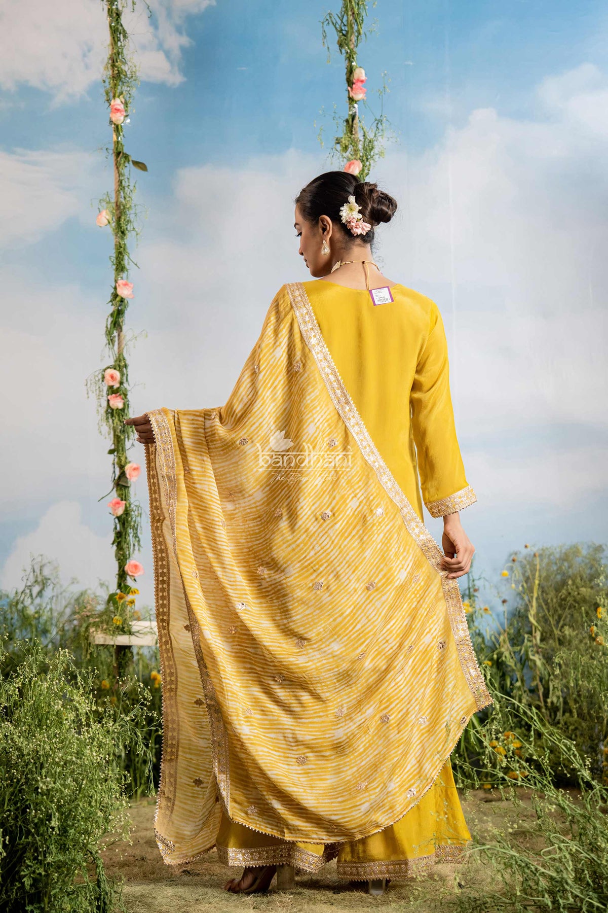 Woman in a yellow saree standing outdoors with a floral swing in the background