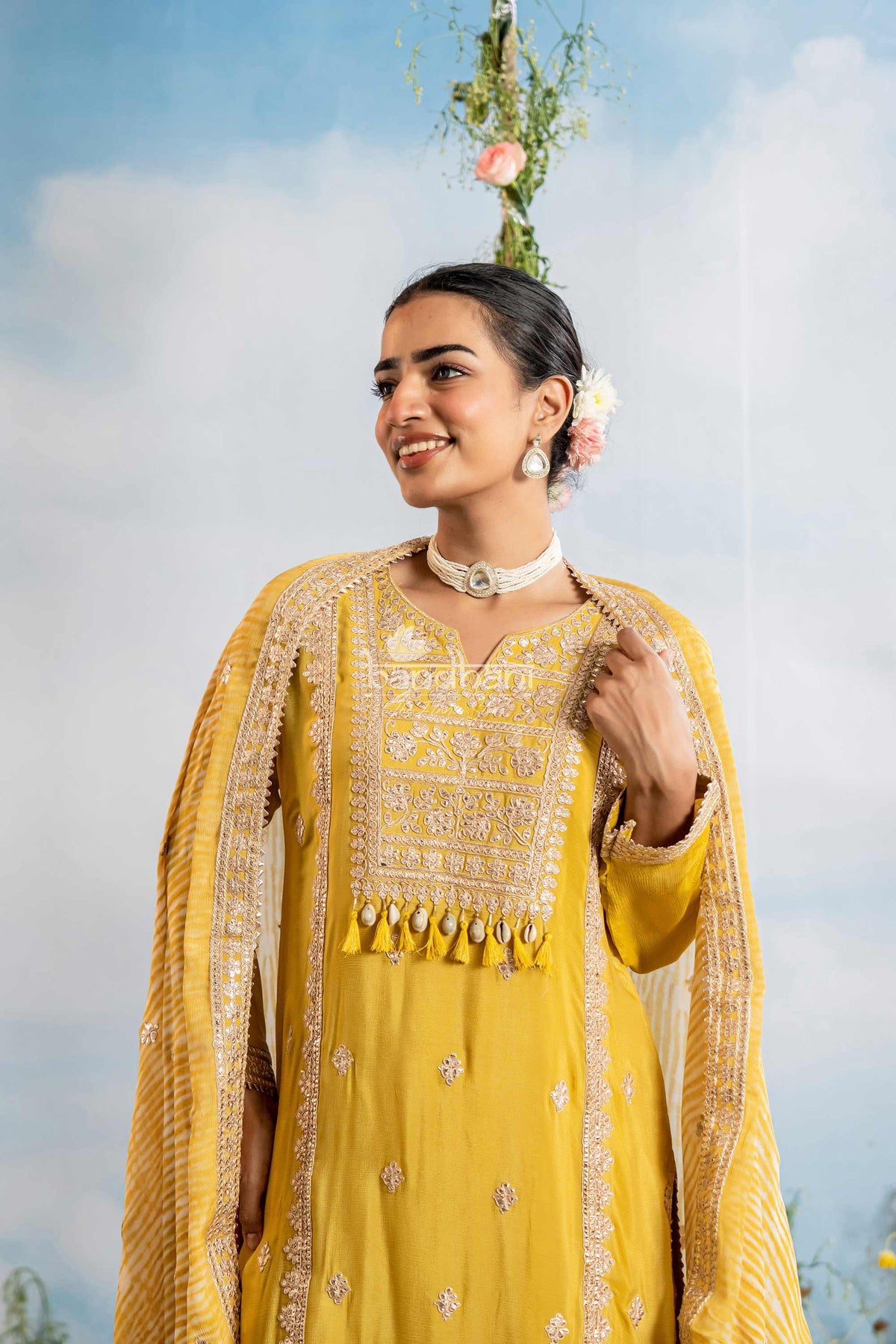 Woman in a yellow traditional outfit with floral decorations against a blue sky.