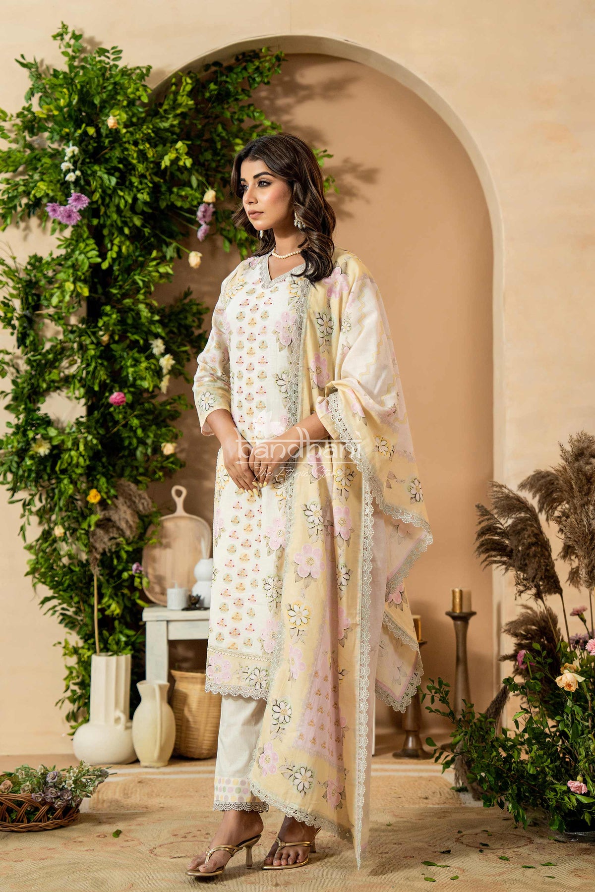 Woman in a traditional outfit standing in a decorated indoor setting with plants and decor.