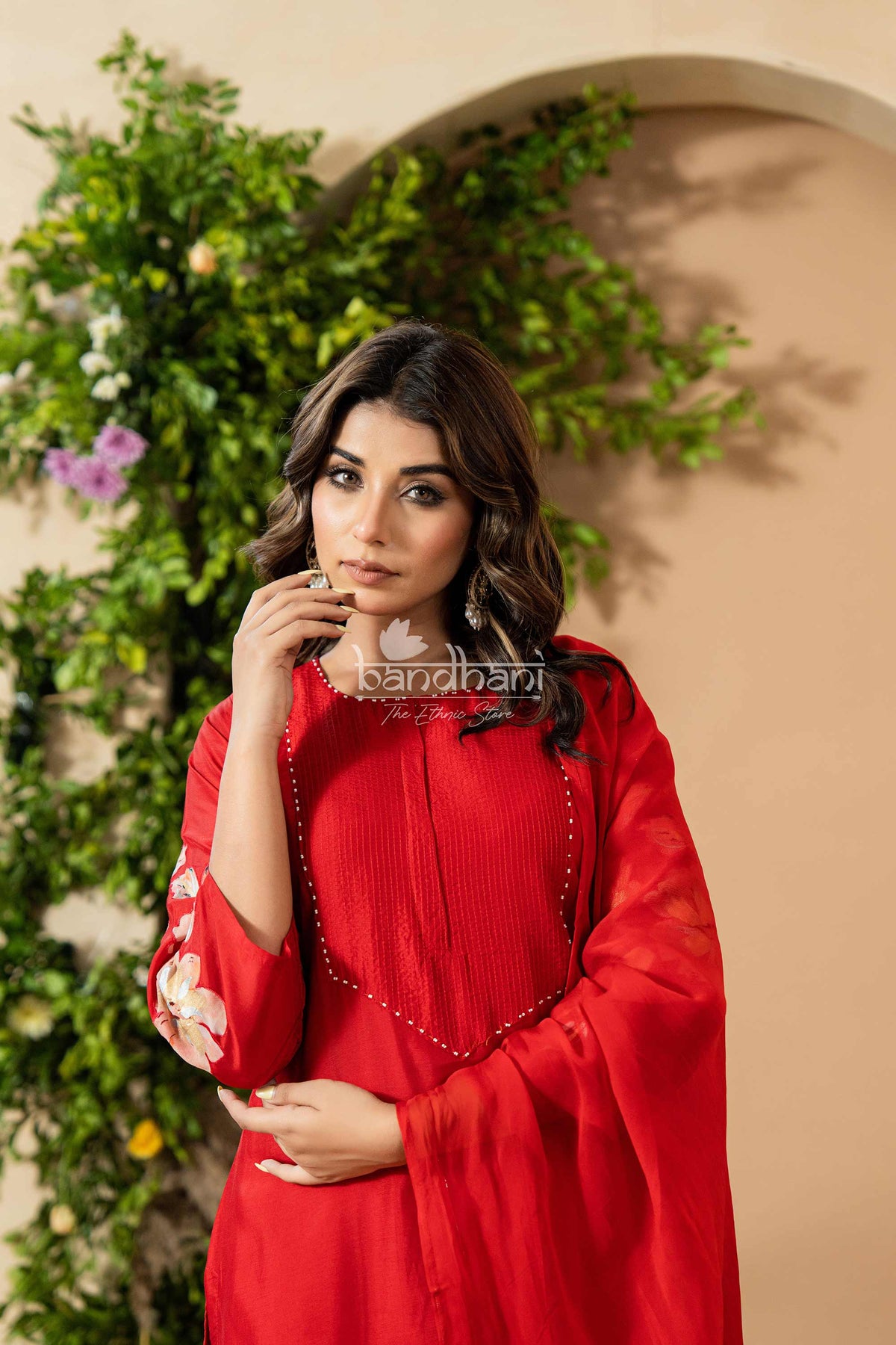 Woman in a red outfit standing against a beige wall with greenery