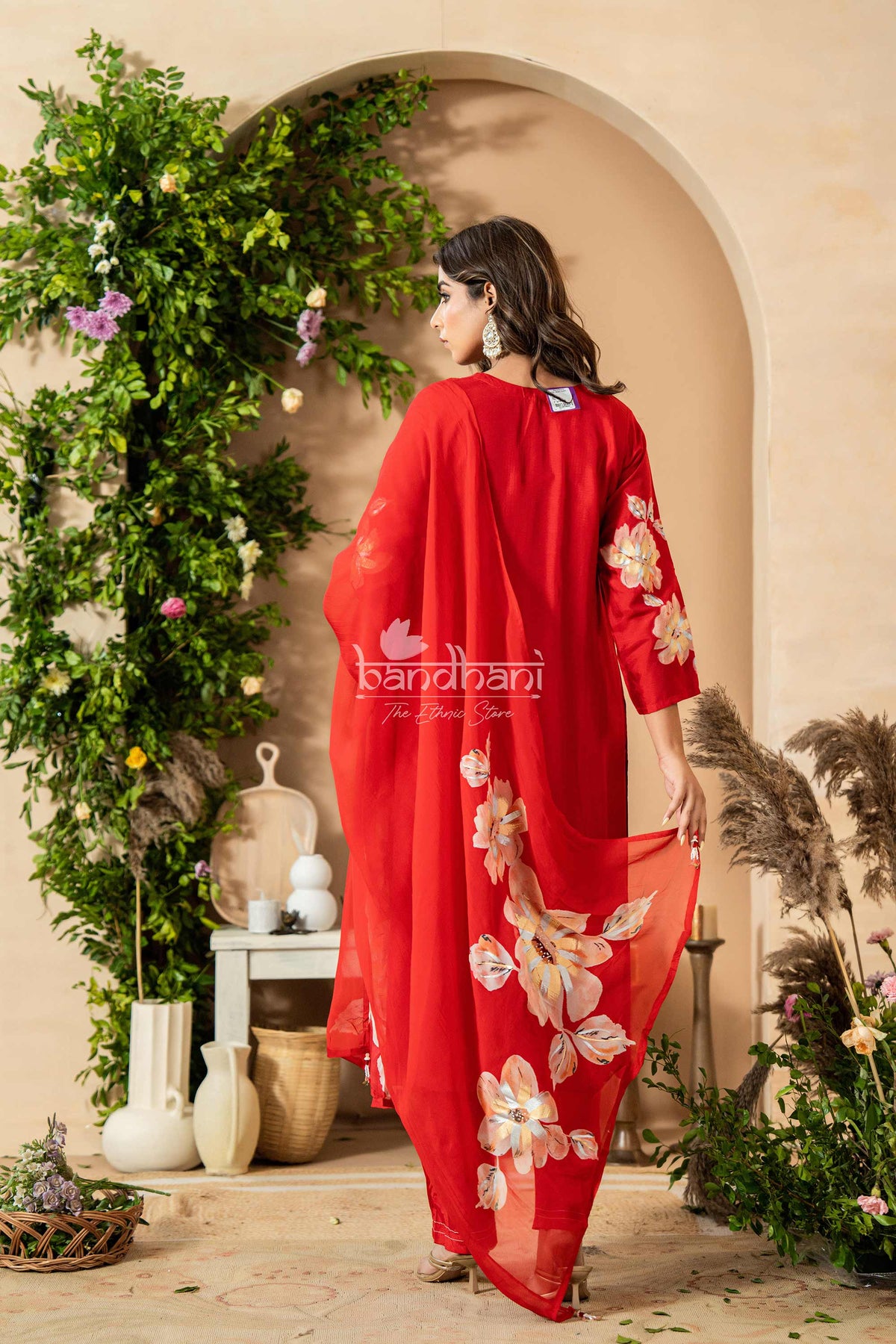 Woman in a red floral outfit standing in front of a decorative arch with plants.