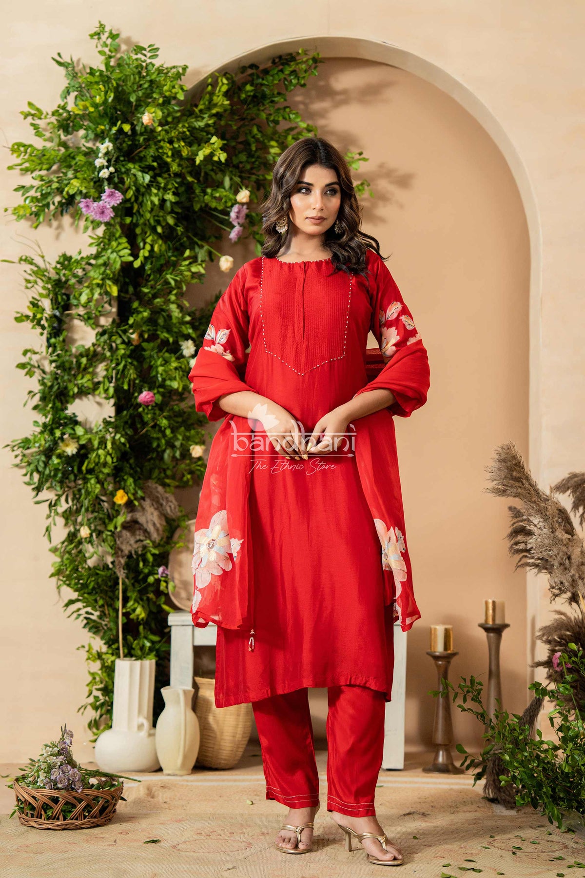Woman in a red traditional outfit standing in front of a decorated archway with greenery.