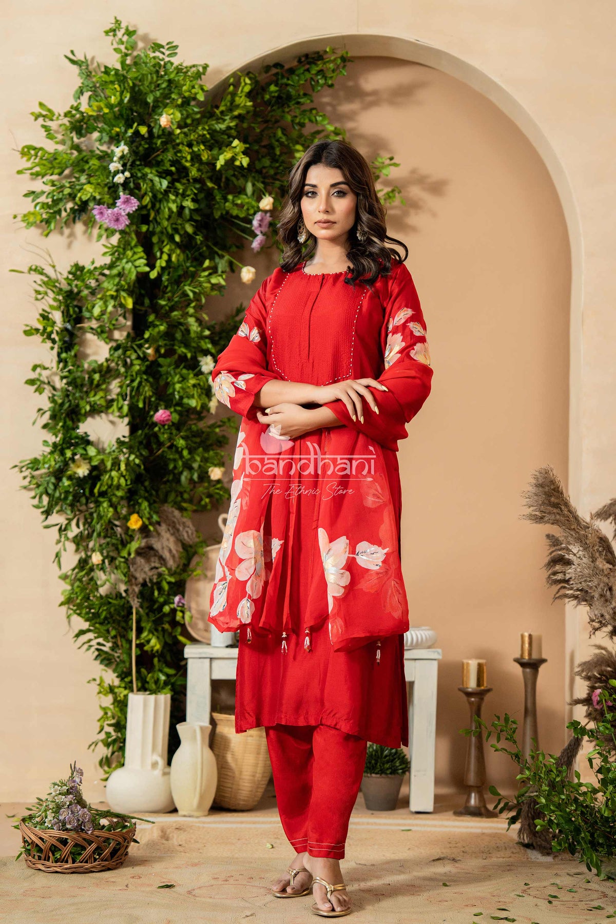 Woman in a red outfit with floral patterns standing in a decorated room.