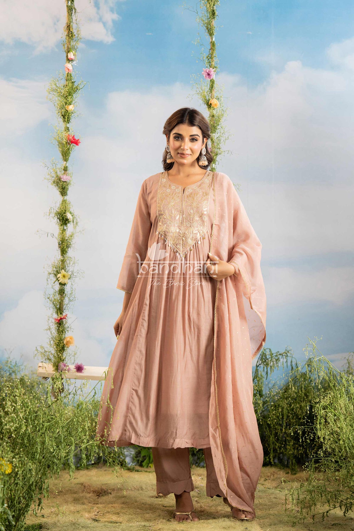 Woman in a pink traditional outfit standing on a grassy area with a floral swing in the background.