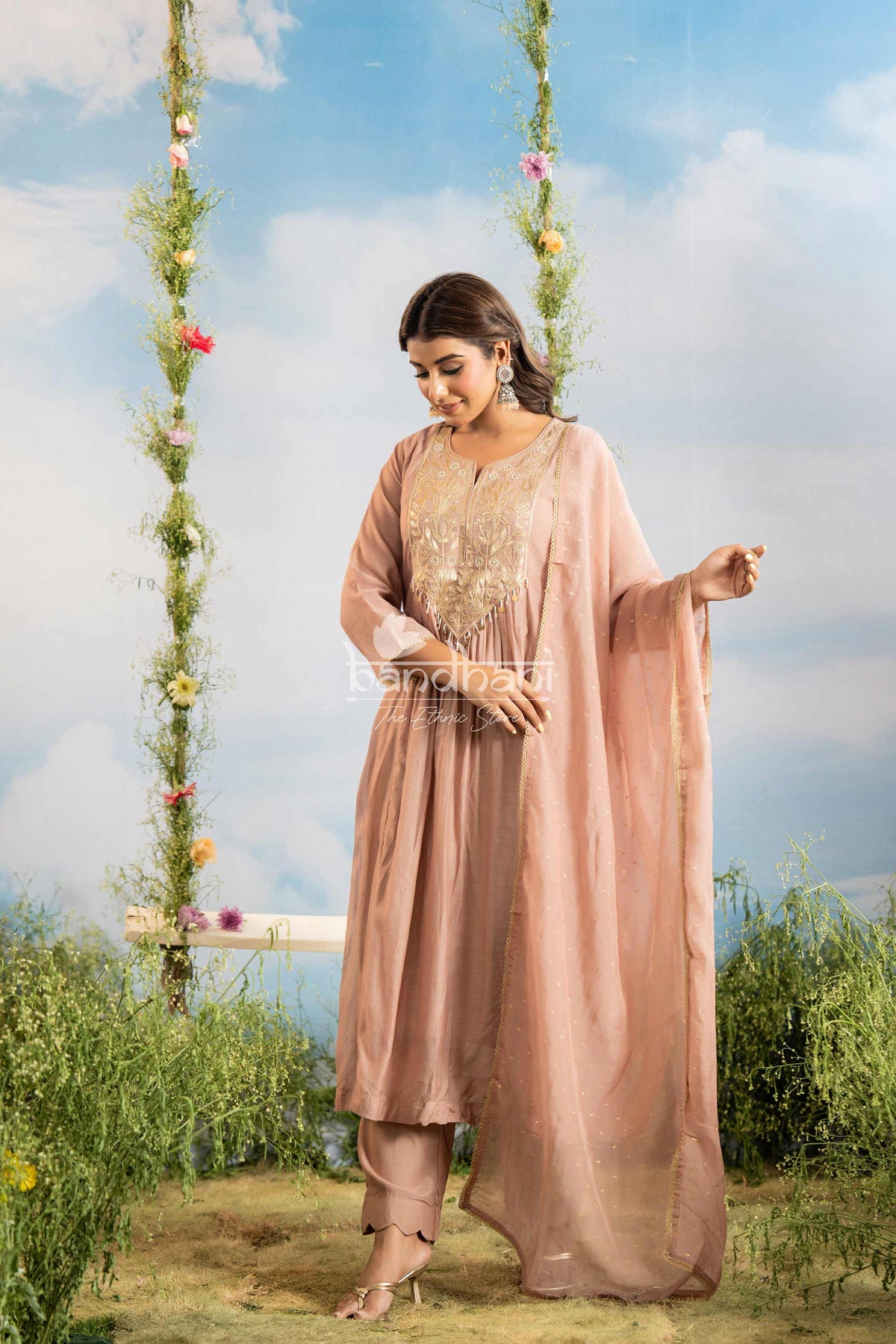 Woman in a pink traditional outfit standing outdoors with greenery and a blue sky background