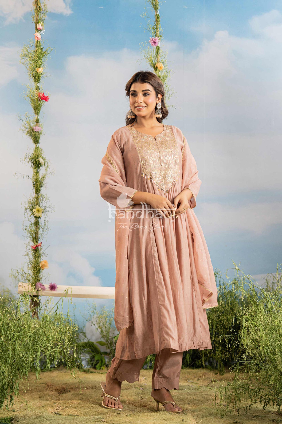 Woman in a pink traditional outfit standing on a grassy area with a decorated swing in the background.