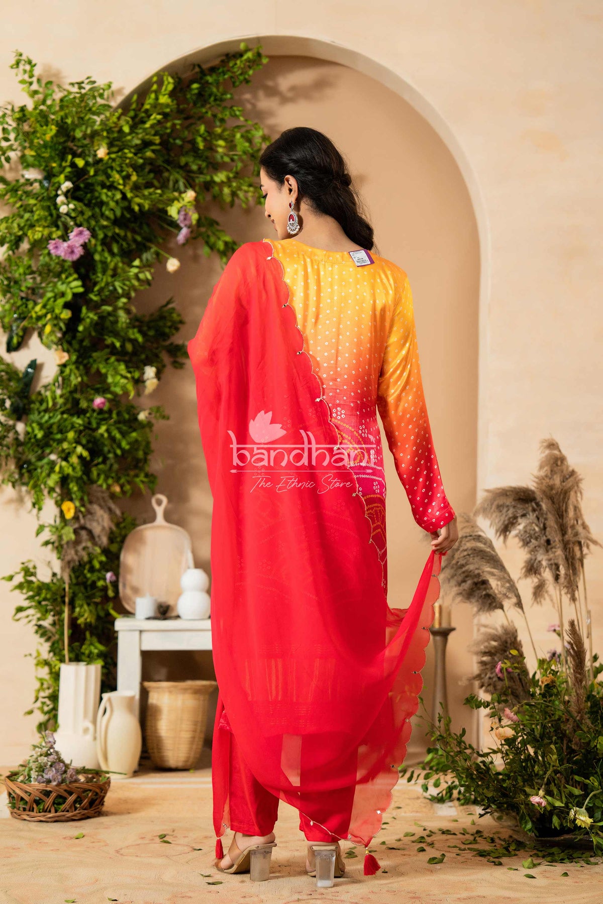 Woman in a red and yellow outfit standing in a decorative setting with plants and archway.