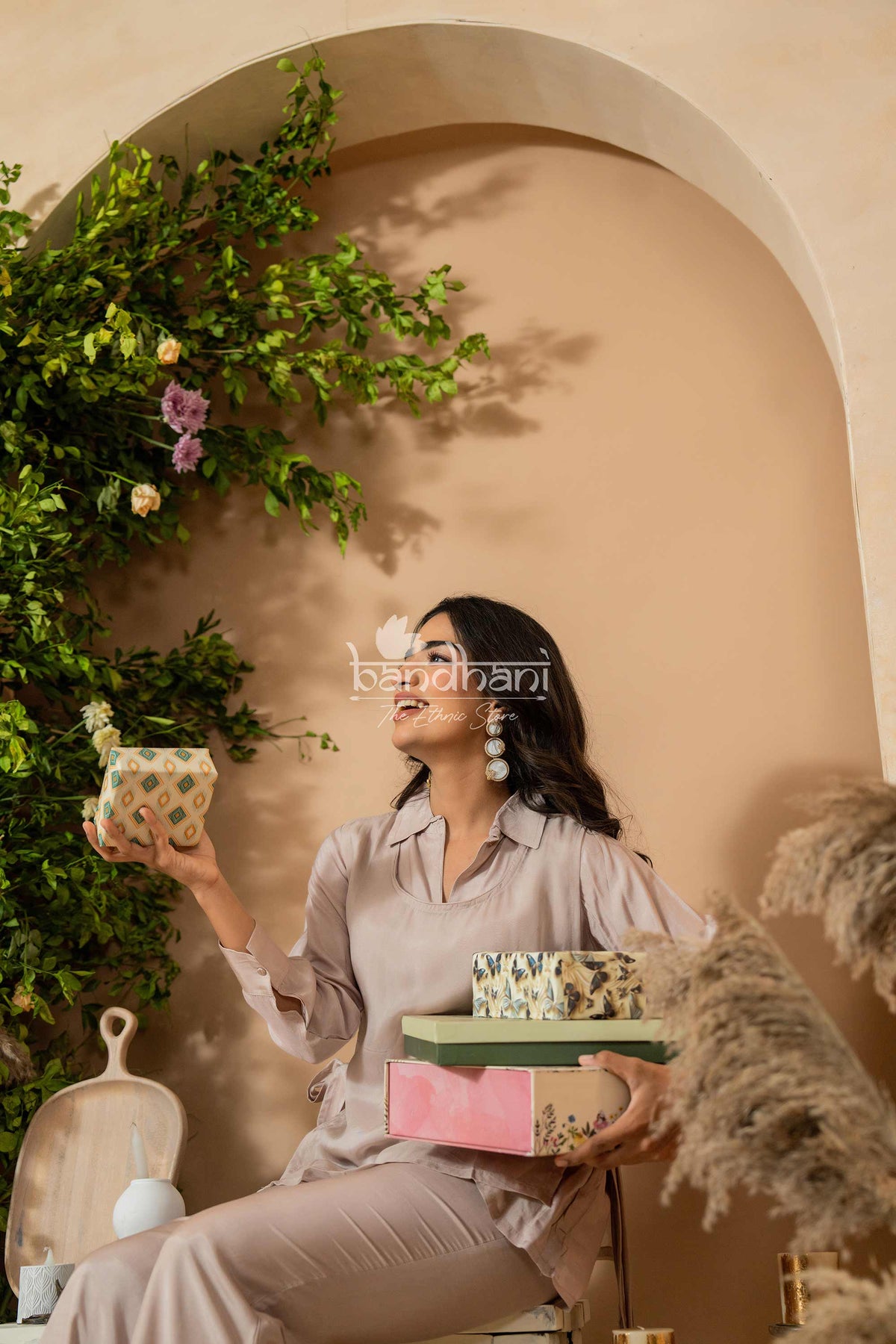 Woman holding decorative boxes against a beige wall with greenery