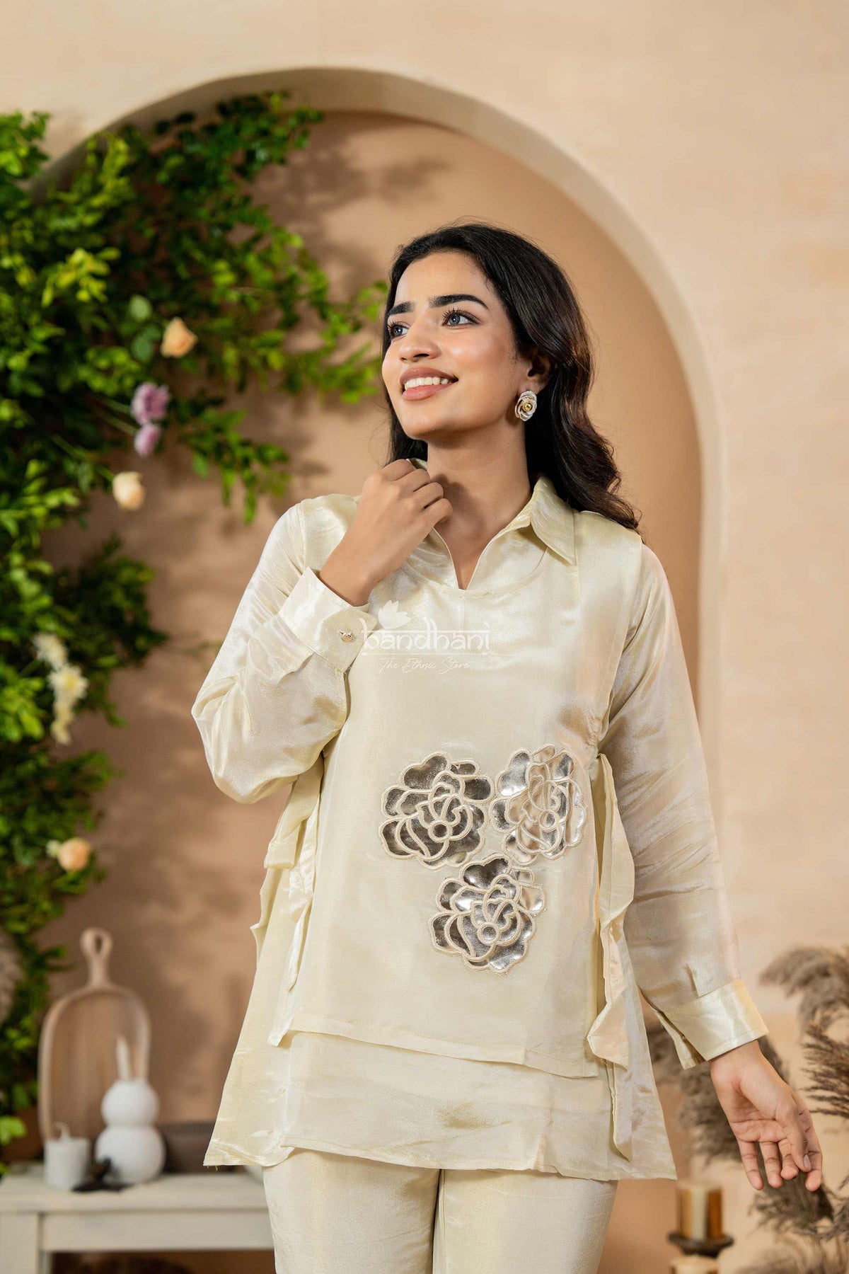 Woman wearing a cream-colored traditional outfit with floral patterns in an outdoor setting.