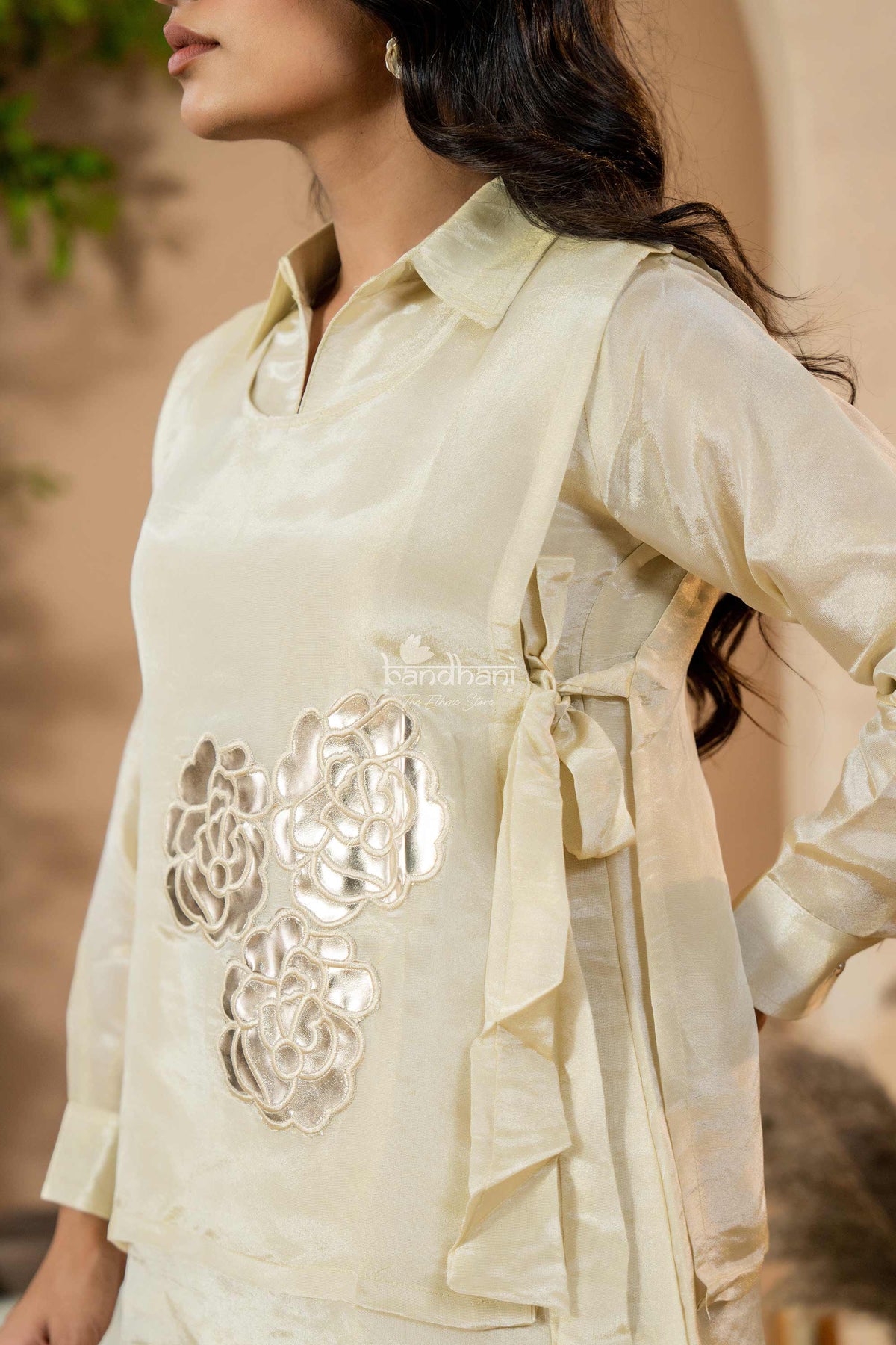 Woman wearing a light-colored outfit with intricate designs, standing against a neutral background.