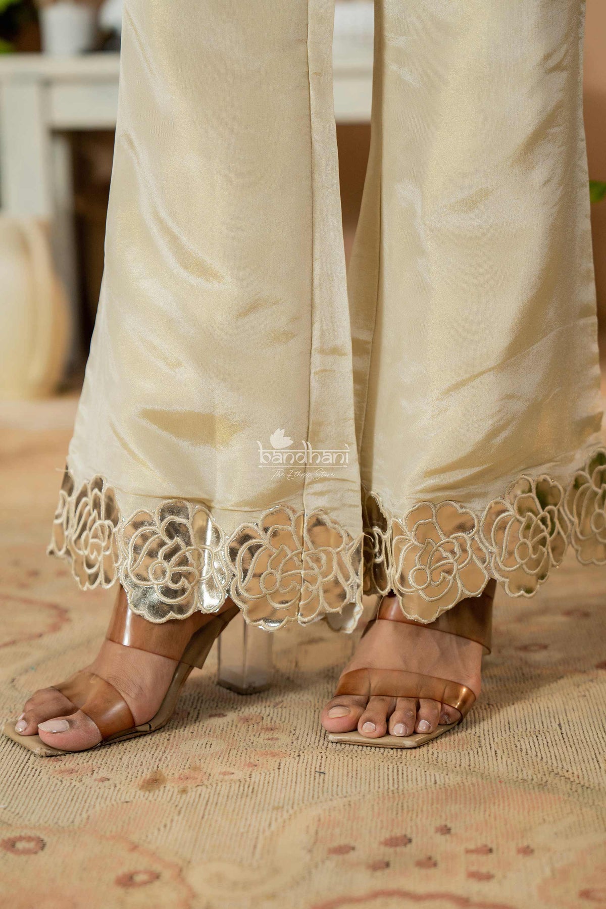 Beige pants with intricate lace hem and brown sandals on a patterned surface.