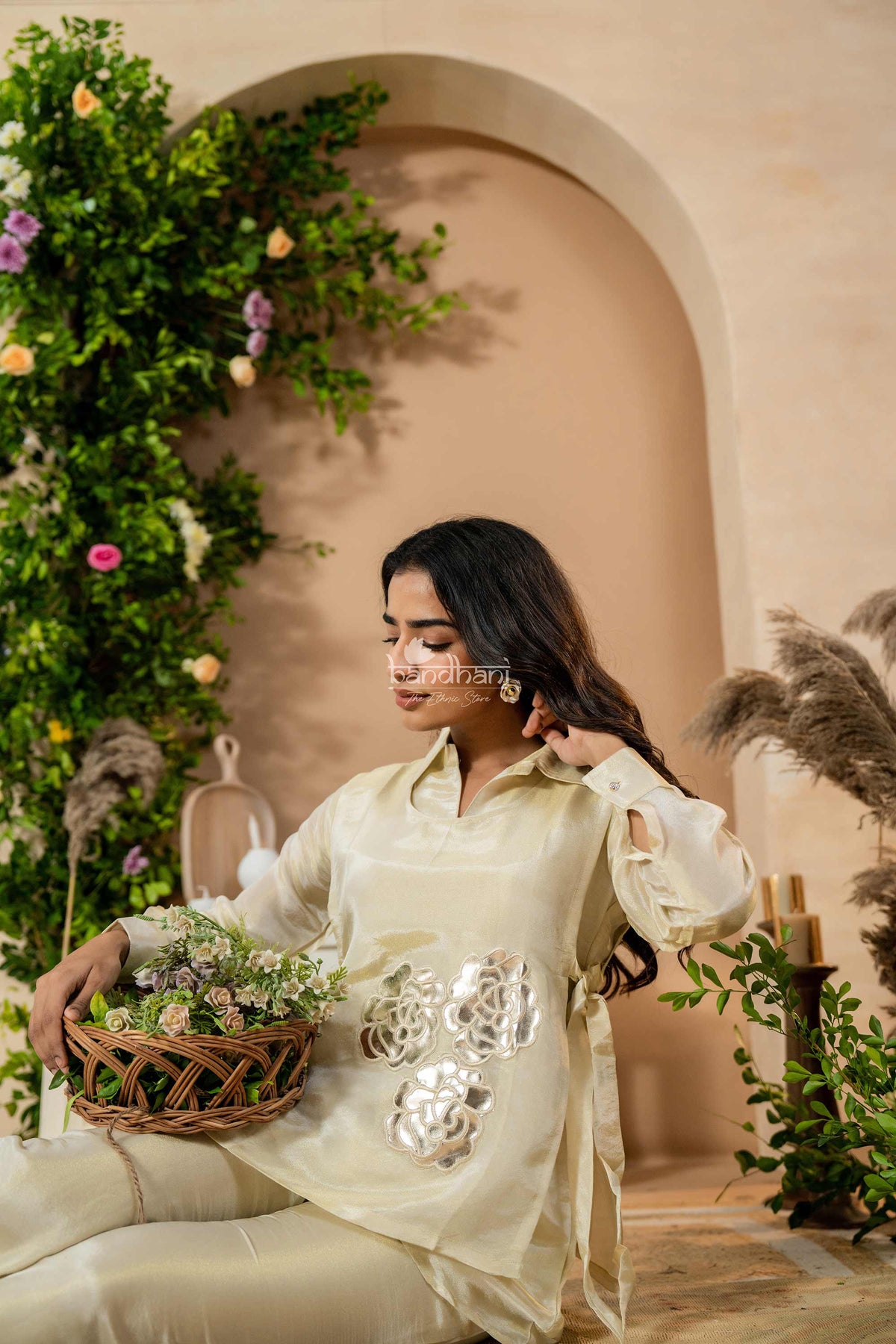 Woman in a light-colored outfit holding a basket of flowers in an outdoor setting with greenery.