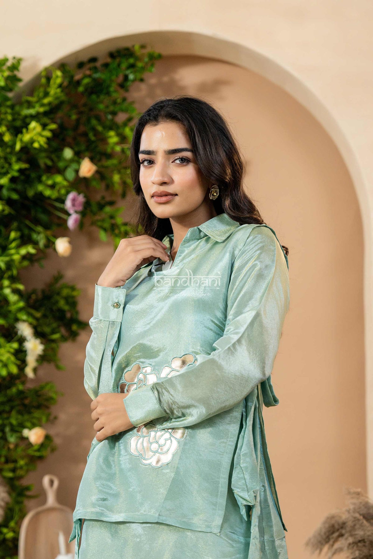 Woman wearing a light green traditional outfit with floral embroidery in an indoor setting.