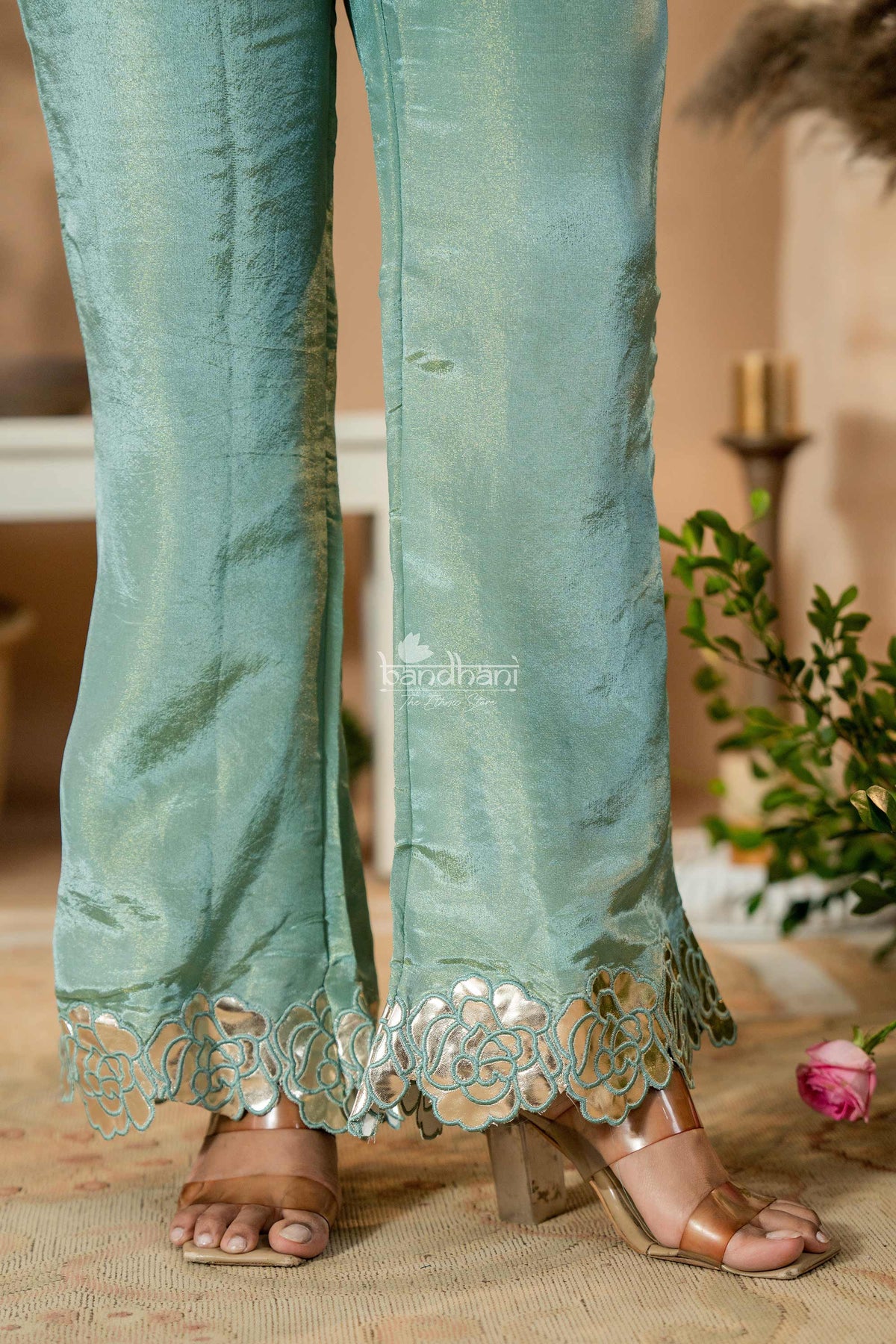 Teal pants with lace detailing worn by a person, blurred background