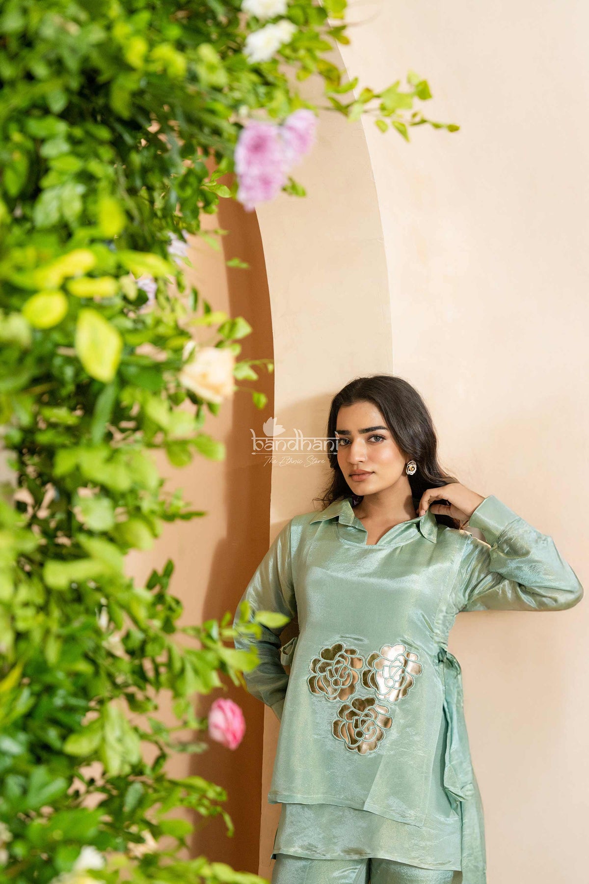 Woman in a green traditional outfit standing next to a floral arch