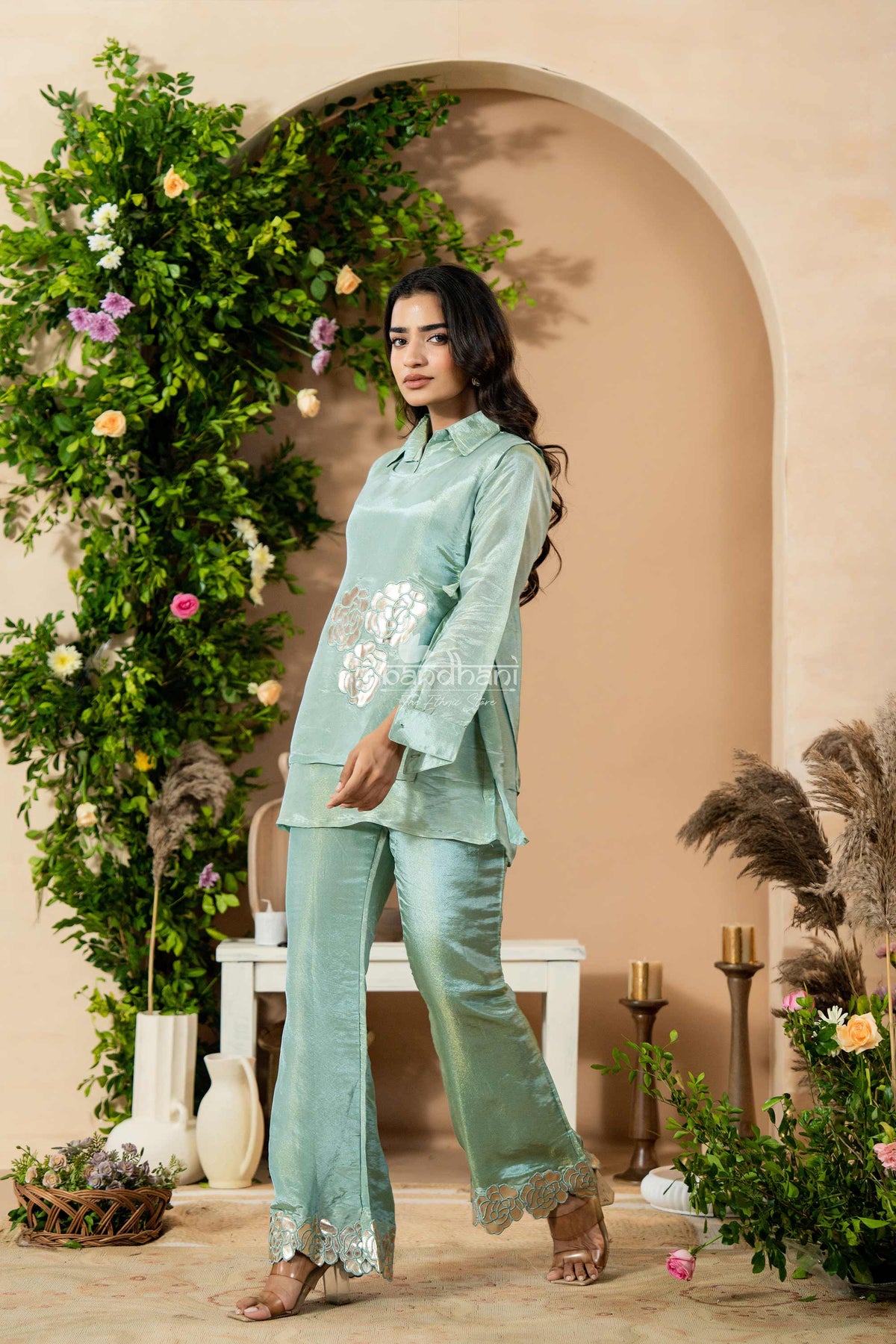 Woman in a light green traditional outfit standing in front of an arch with floral decorations.