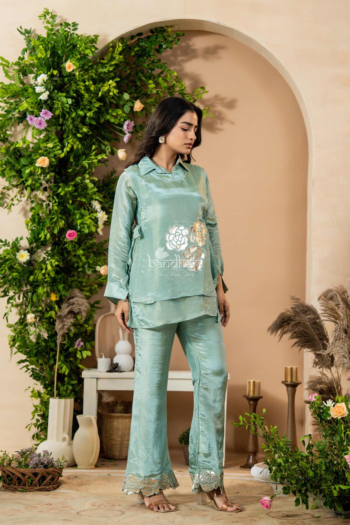 Woman wearing a green outfit with floral patterns in a decorated indoor setting.