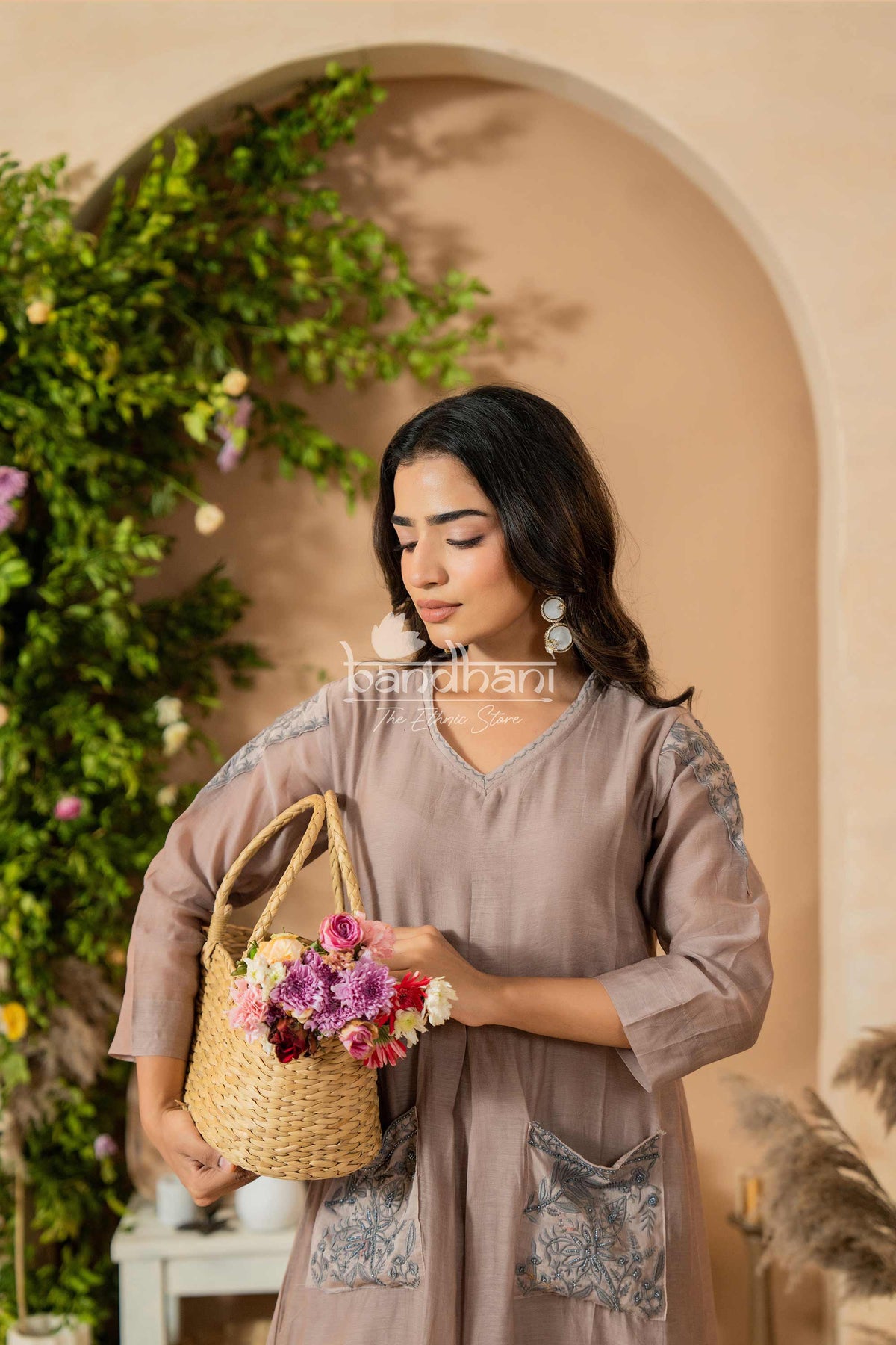 Woman holding a woven basket with flowers against a decorative archway.