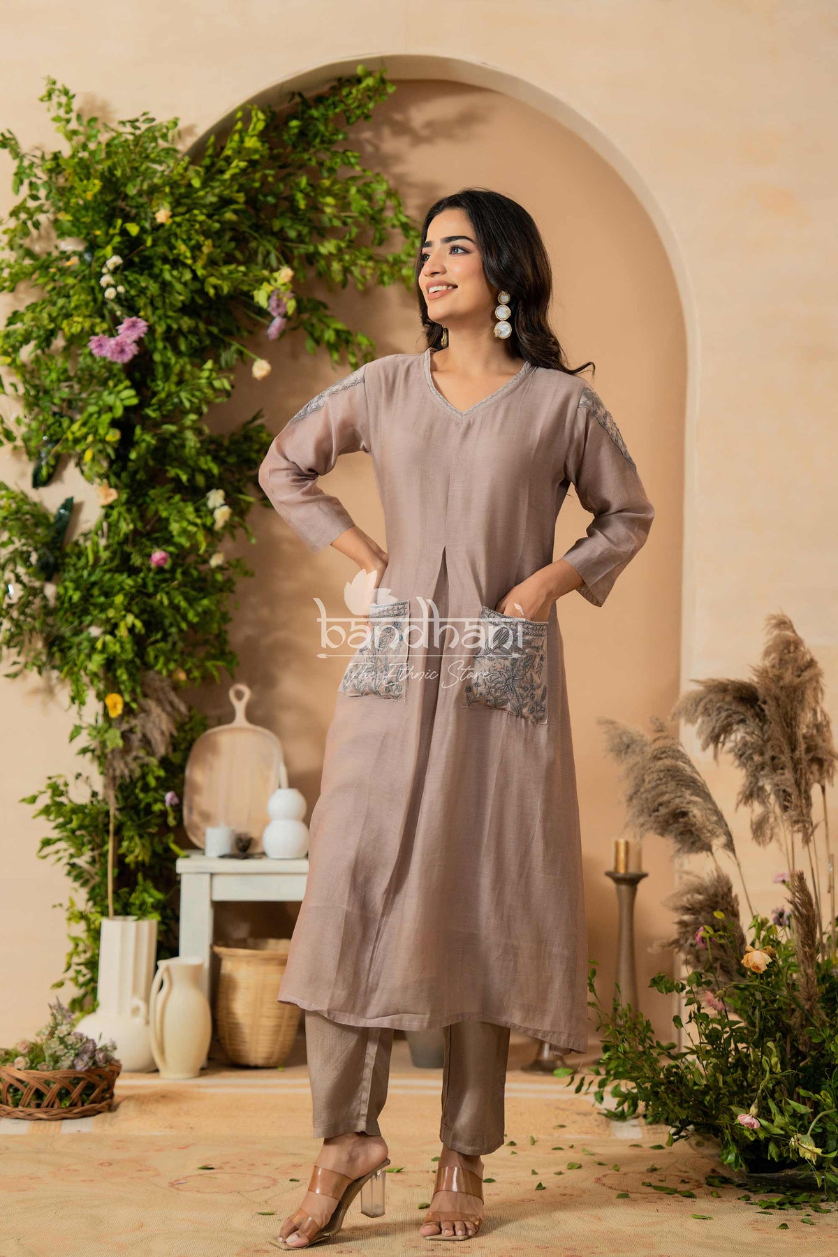 Woman in a gray outfit standing in a decorated indoor setting with plants and decor.