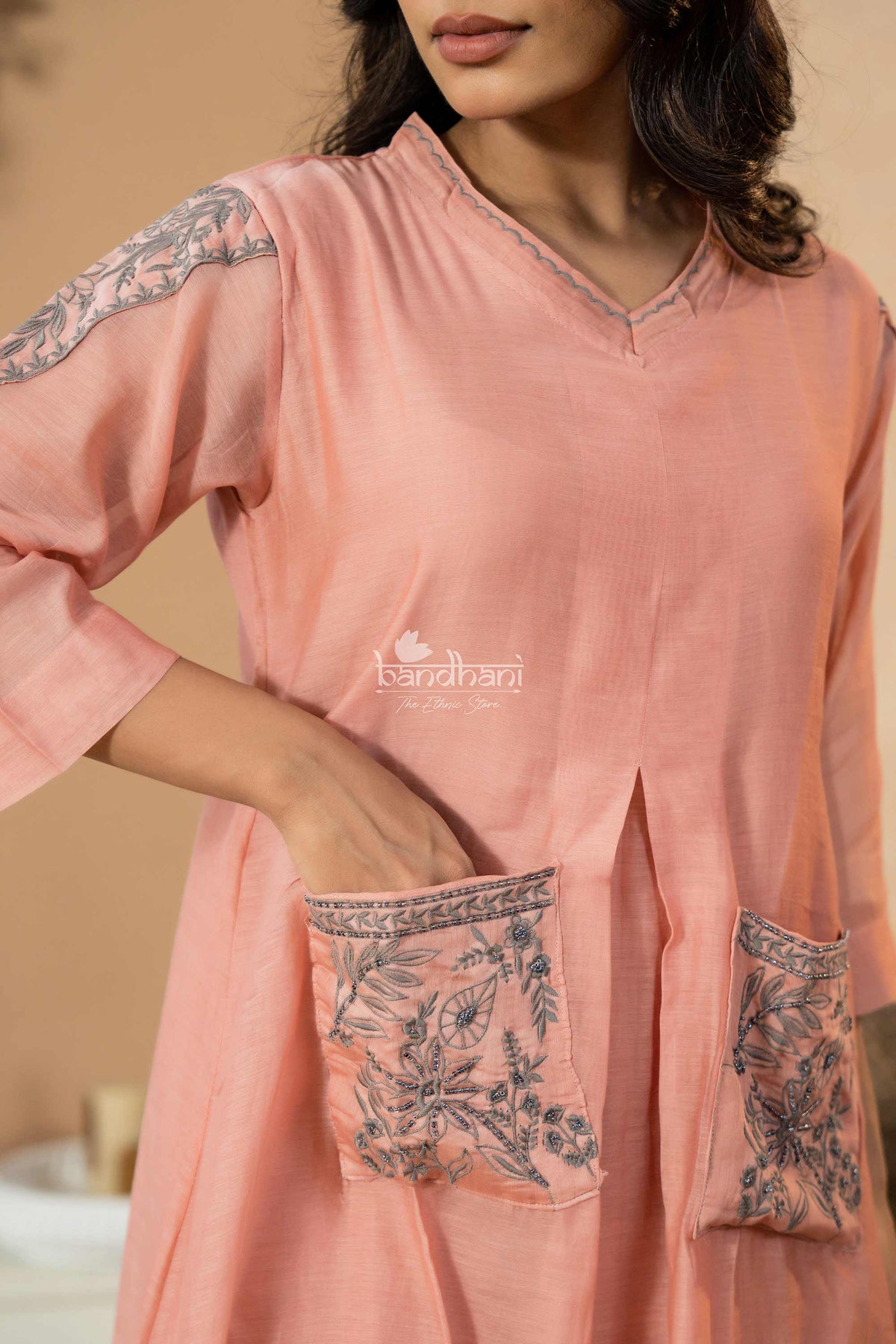Woman wearing a peach-colored kurta with floral embroidery on a beige background